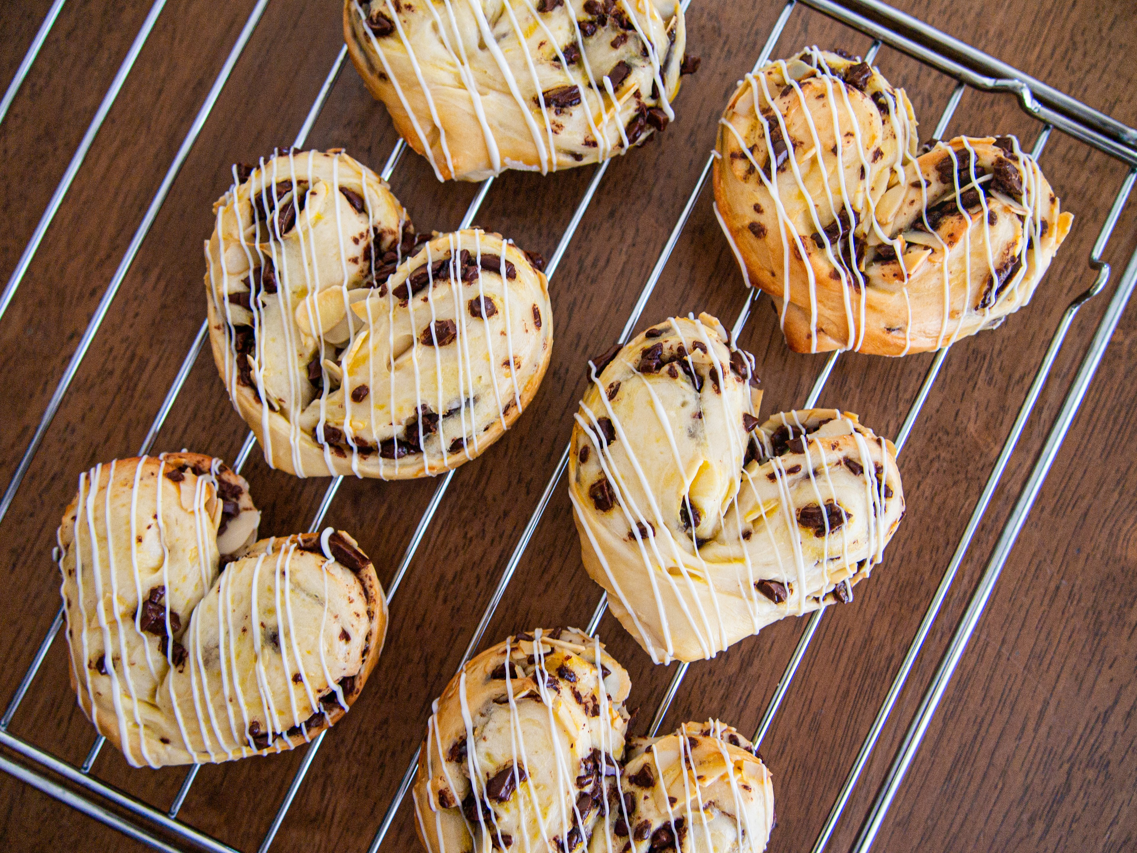 Heart-shaped pastries with chocolate chips and icing on a cooling rack