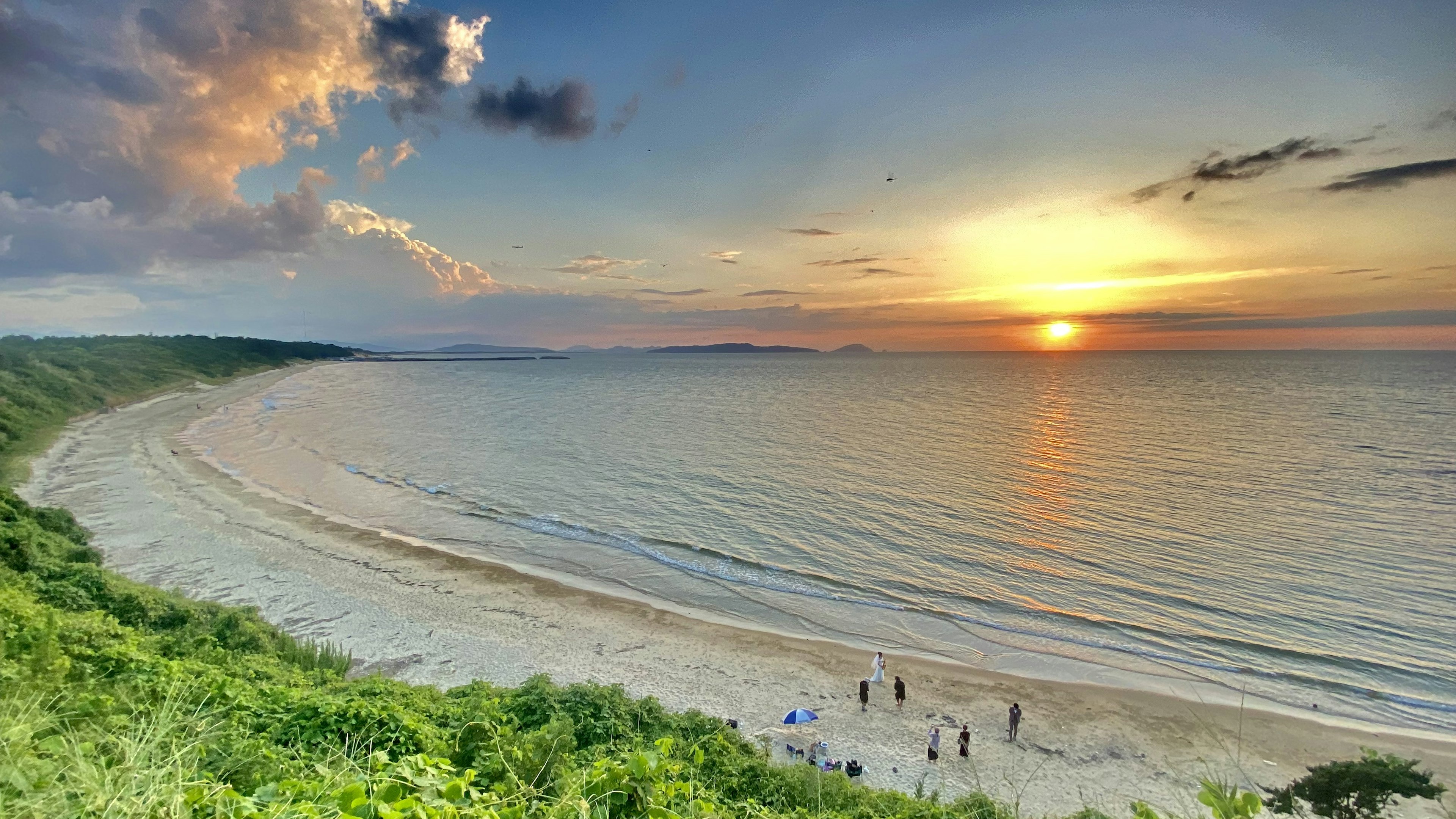 Scenic view of a sunset over the ocean with a beach and green foliage