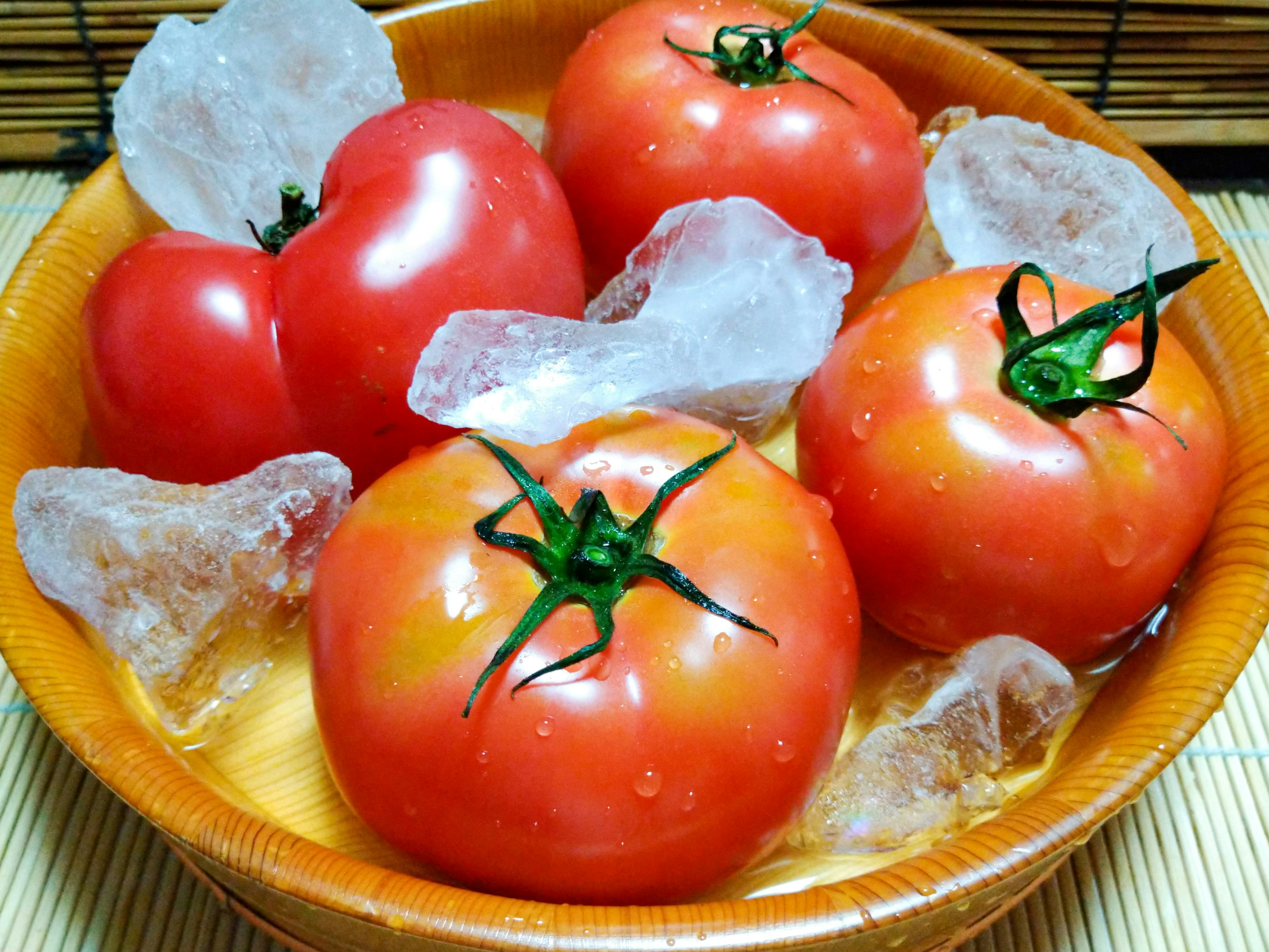 Pomodori freschi immersi in ghiaccio e acqua in una ciotola di legno