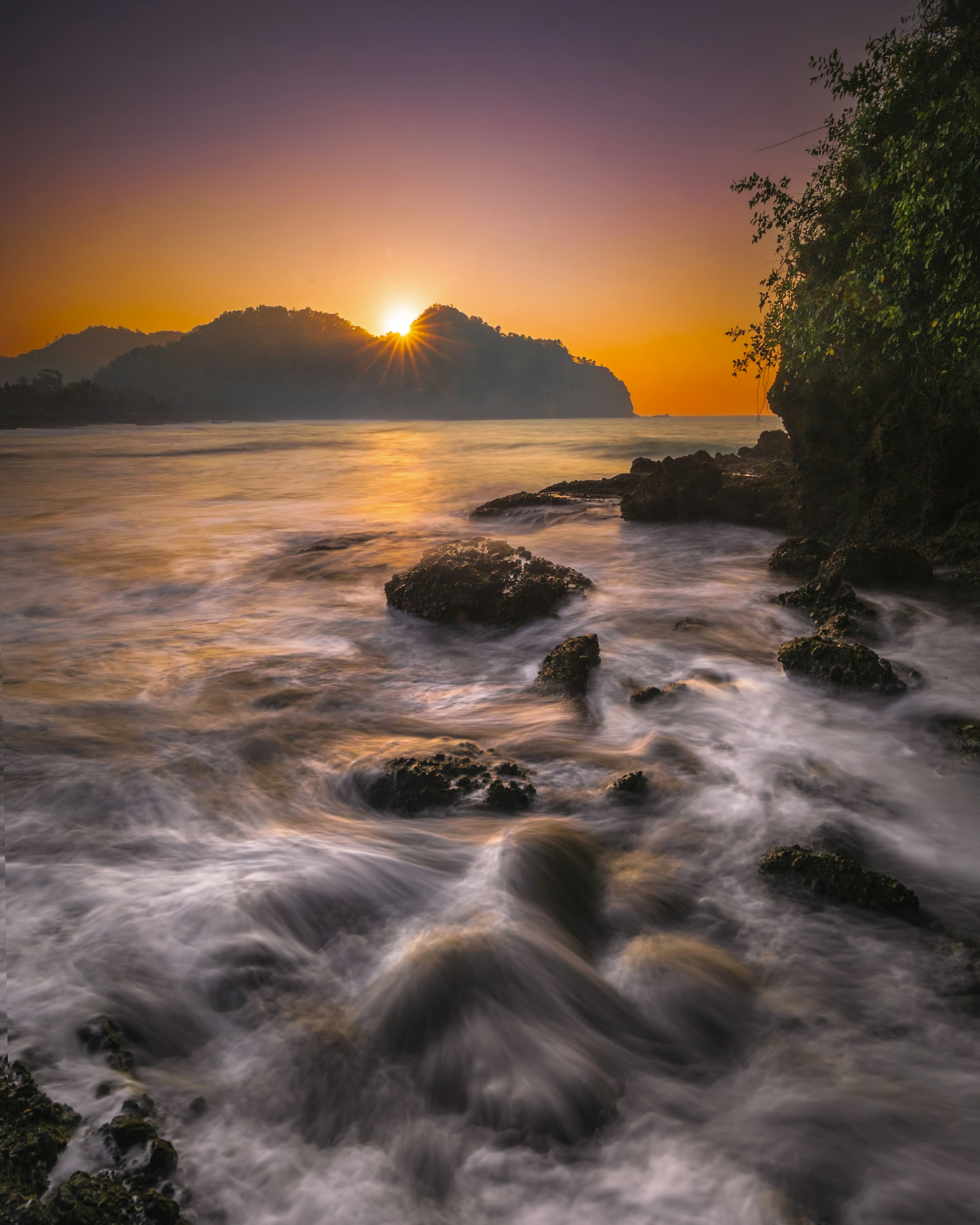 Pemandangan pantai saat matahari terbenam dengan ombak dan batuan