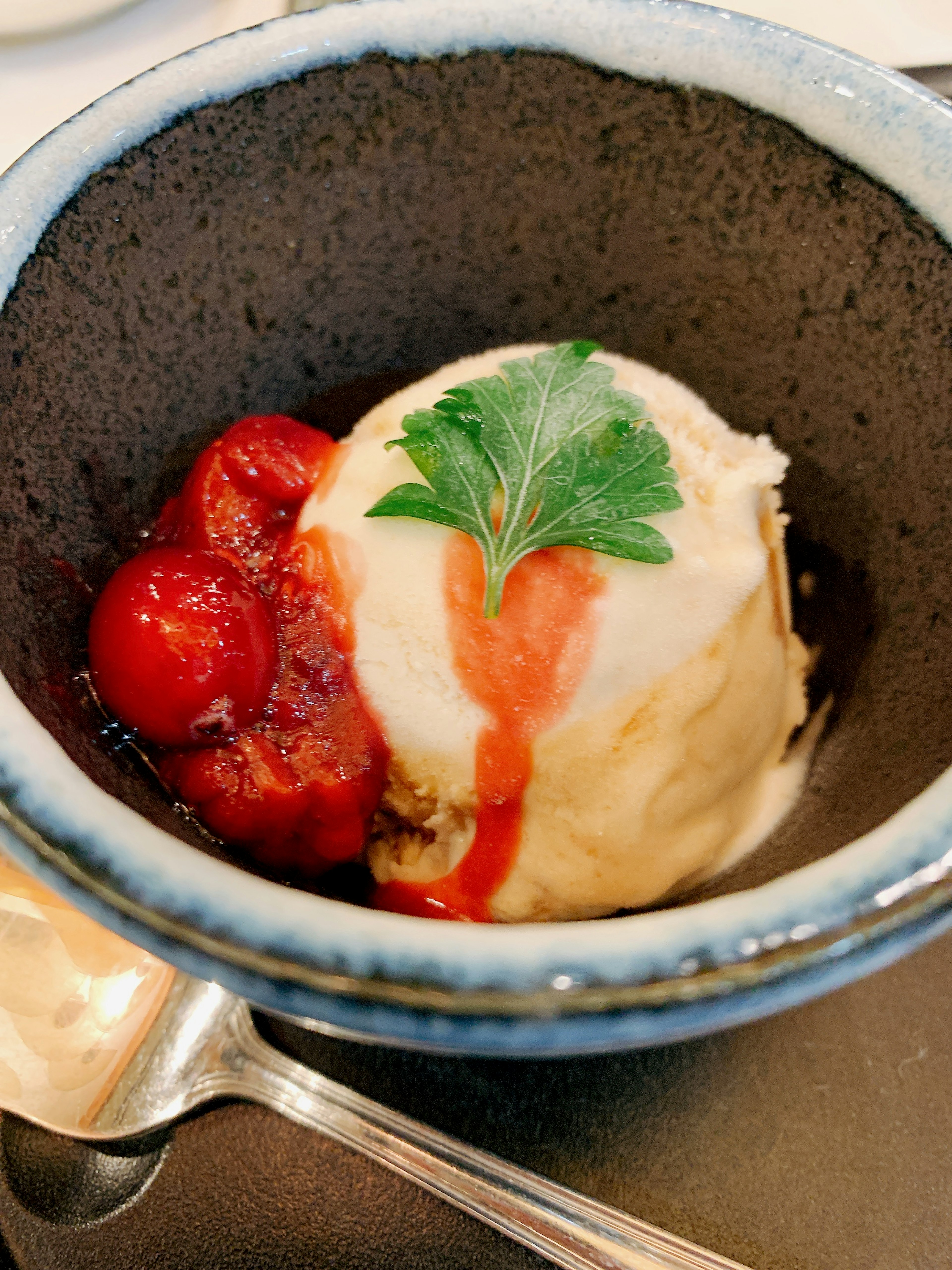 Dessert in einer schwarzen Schüssel mit roten Früchten und einer grünen Garnitur serviert