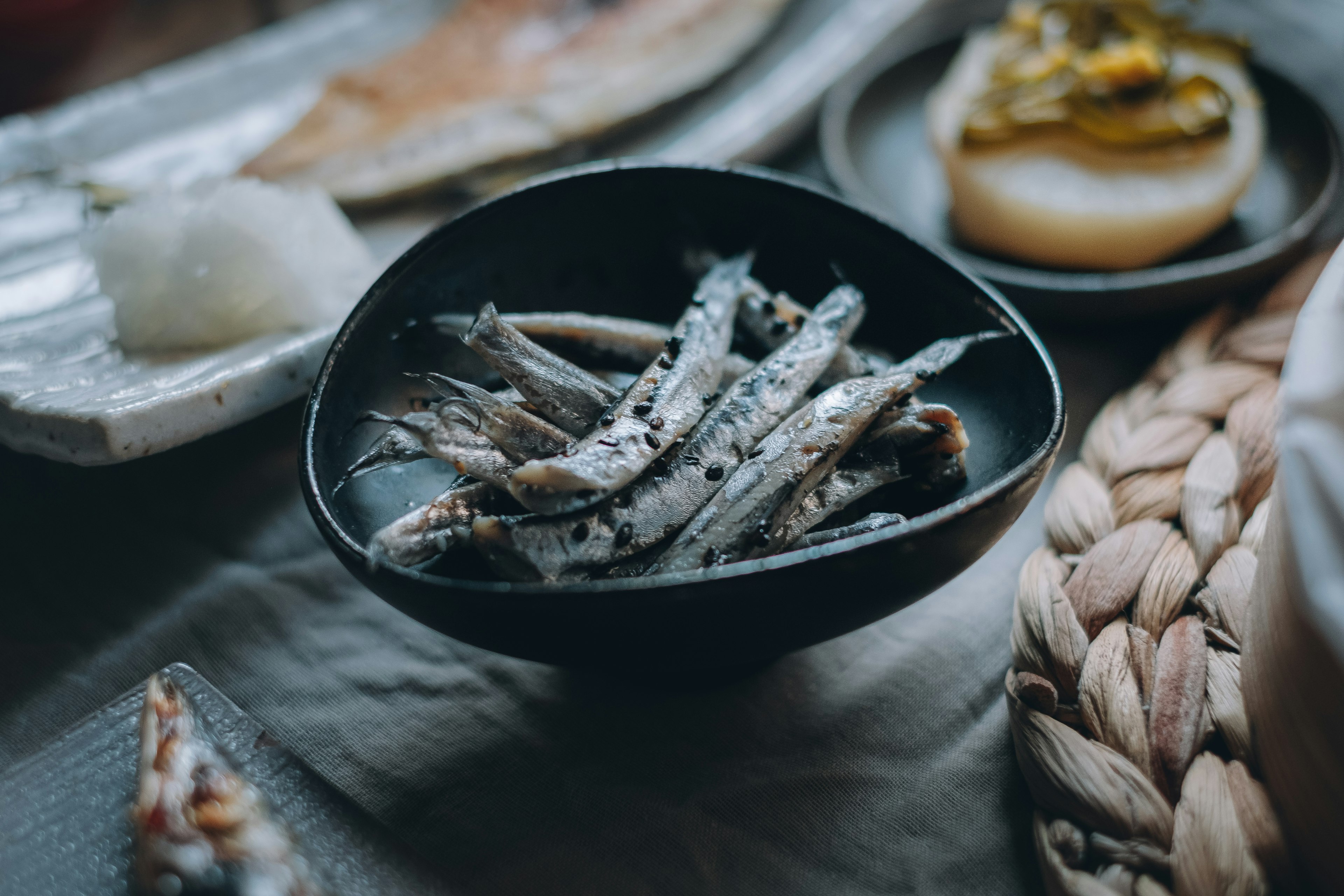 Small fish dish in a black bowl with surrounding Japanese cuisine