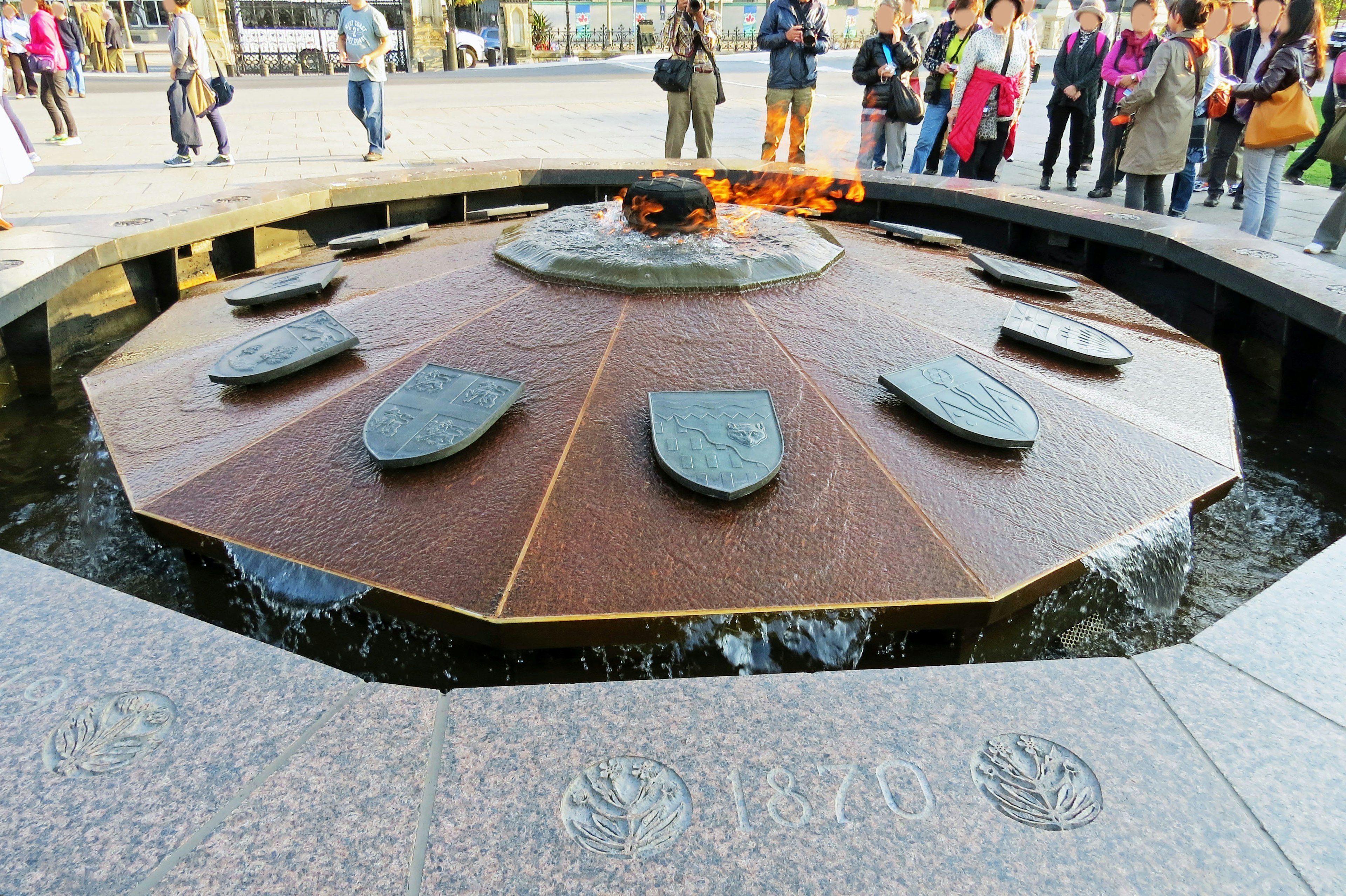 Octagonal fountain with a burning flame and surrounding tourists