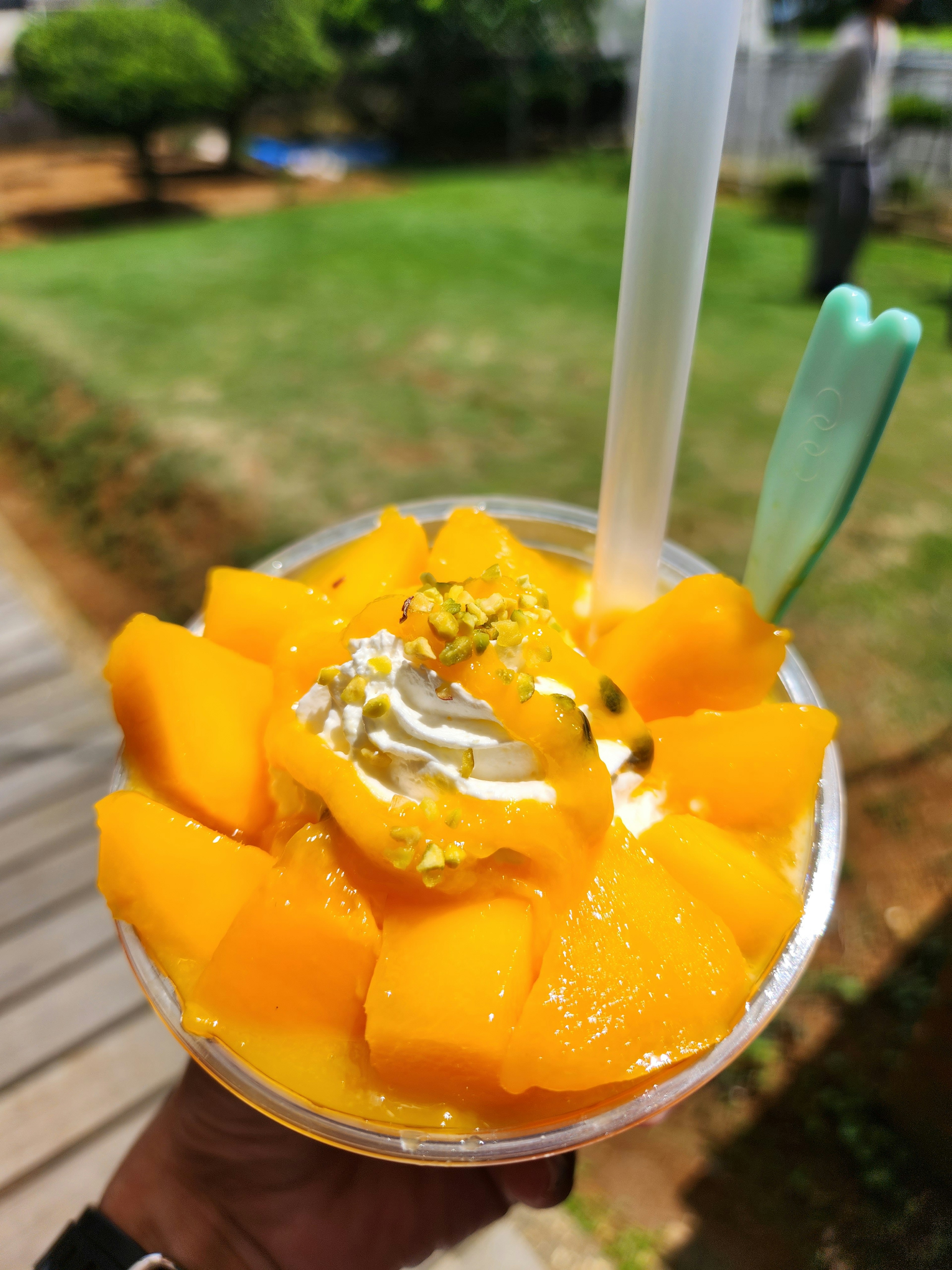 Vaso de mango en cubos cubierto con crema batida y una pajita verde