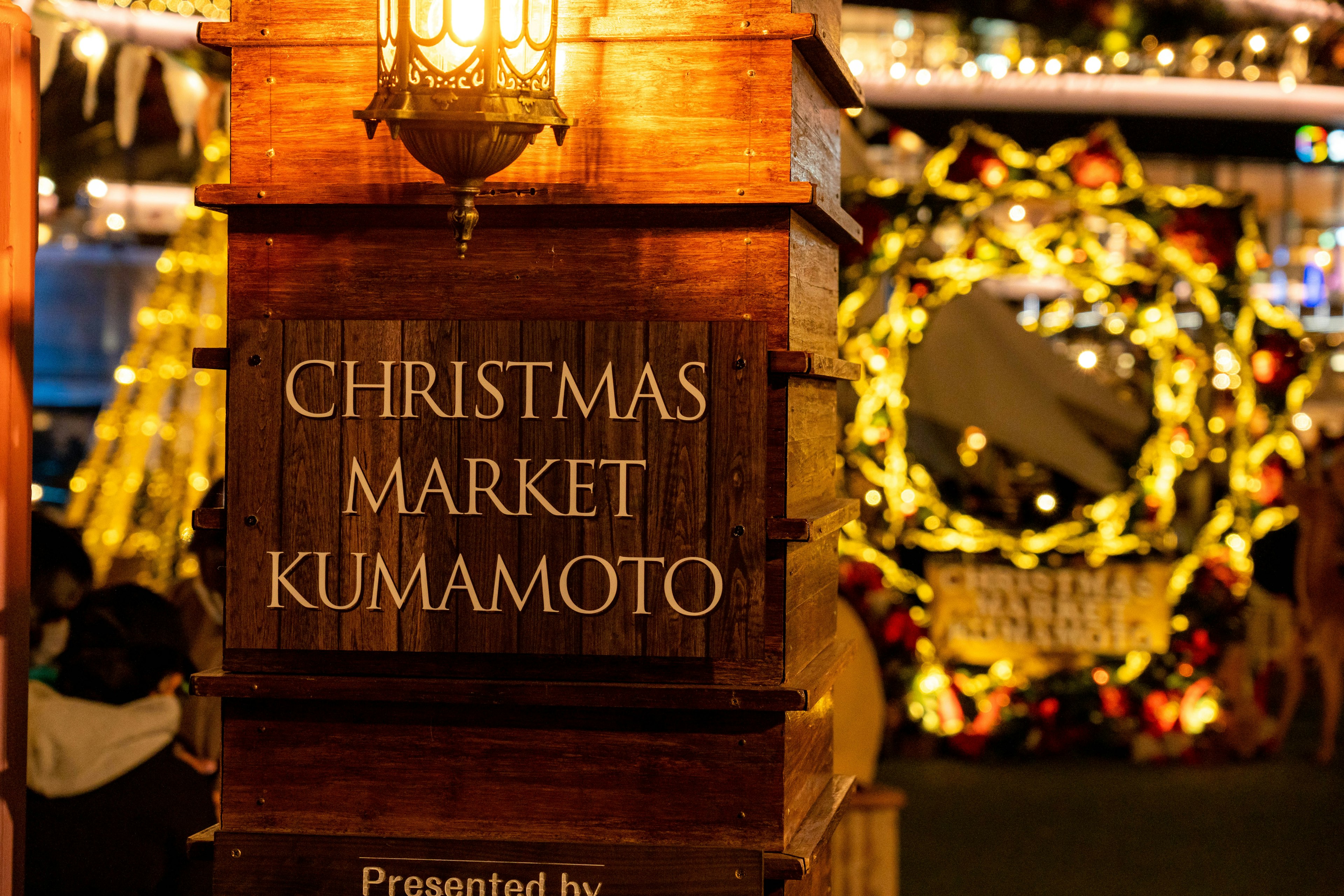 Cartel de madera para el Mercado de Navidad de Kumamoto con decoraciones festivas de fondo