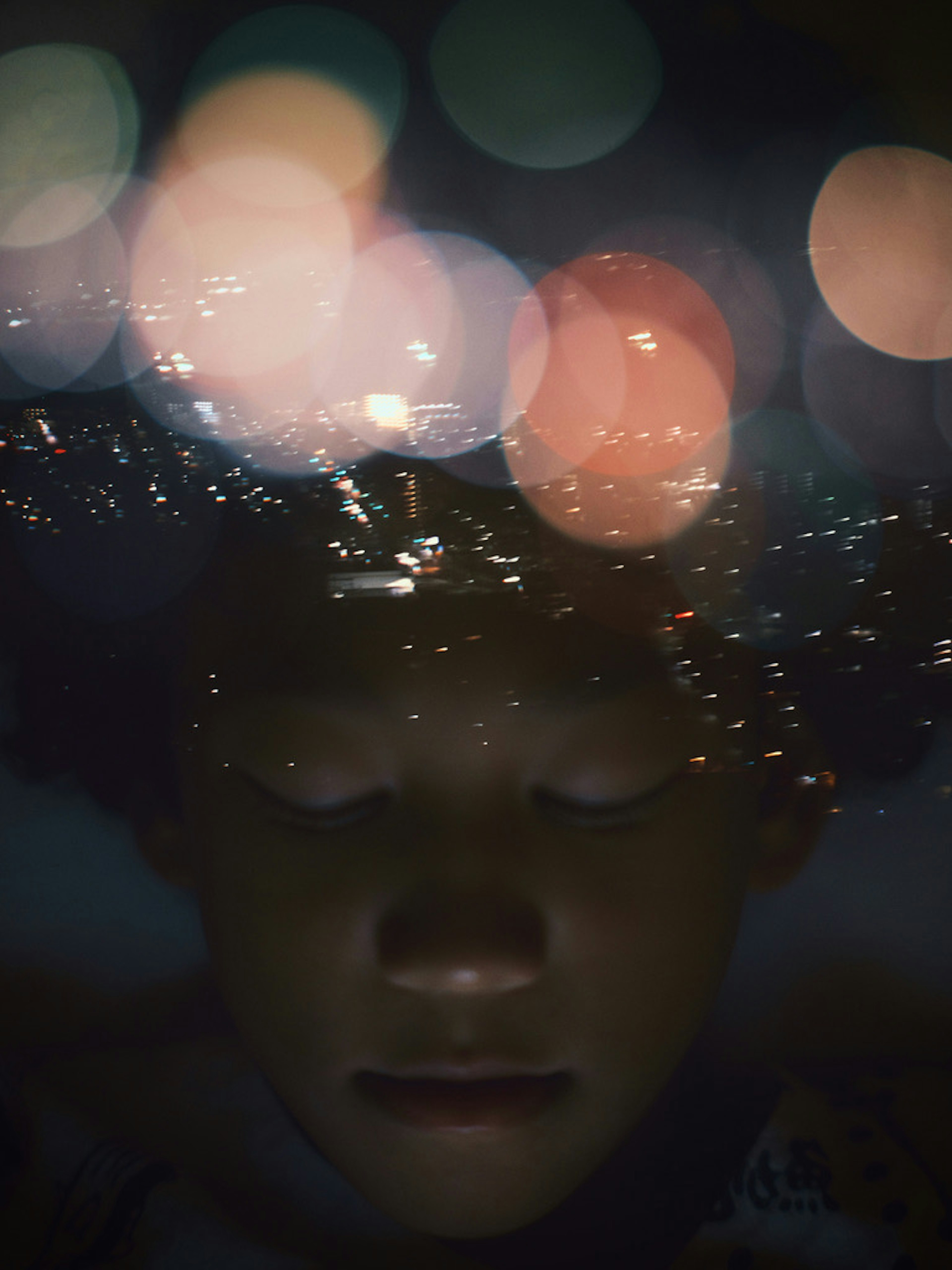 A boy's face enveloped by a blurred city skyline and lights