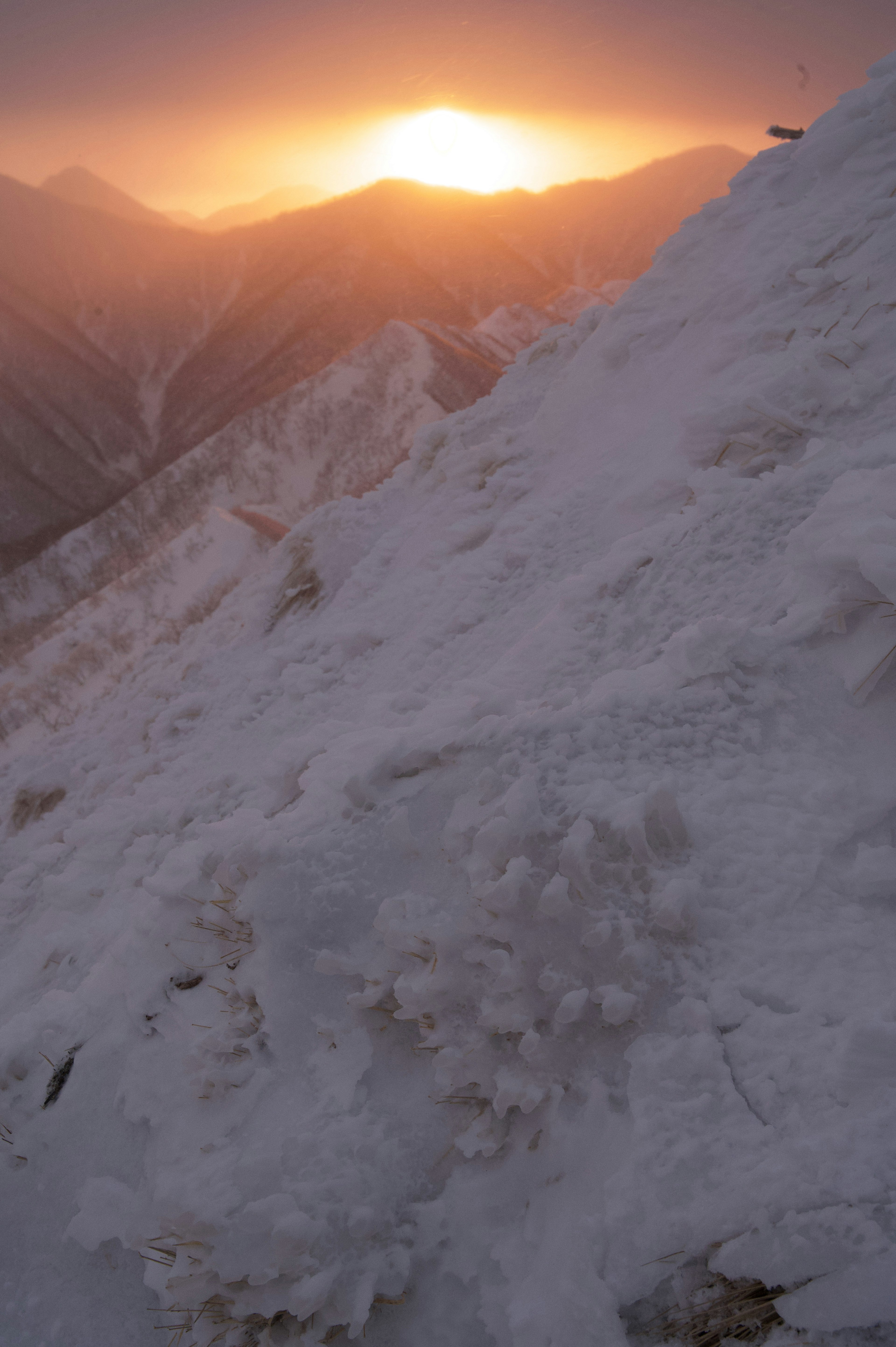 雪に覆われた山の斜面と夕日の光