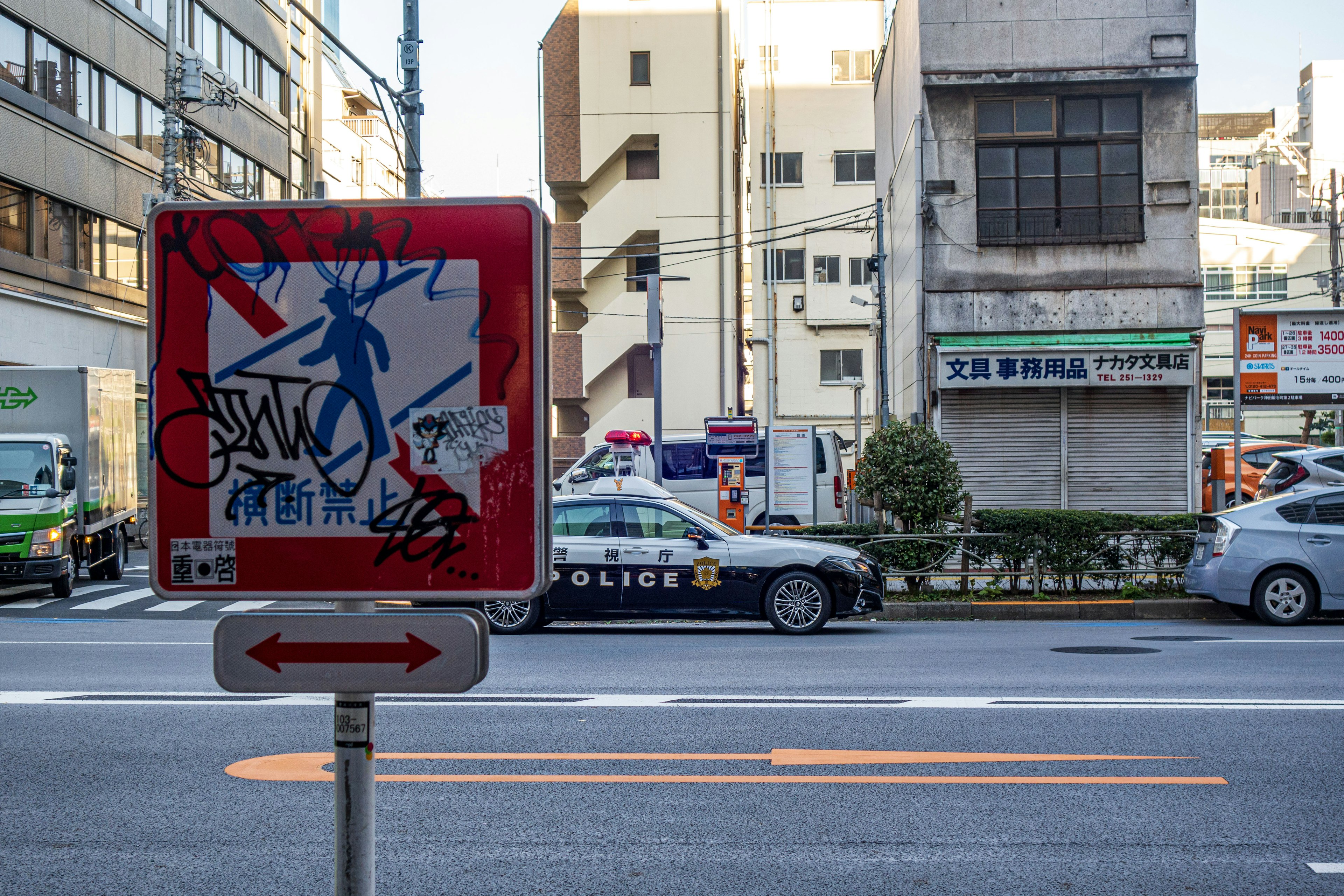 赤い標識と落書きのある通りの風景 警察車両とビルが並ぶ