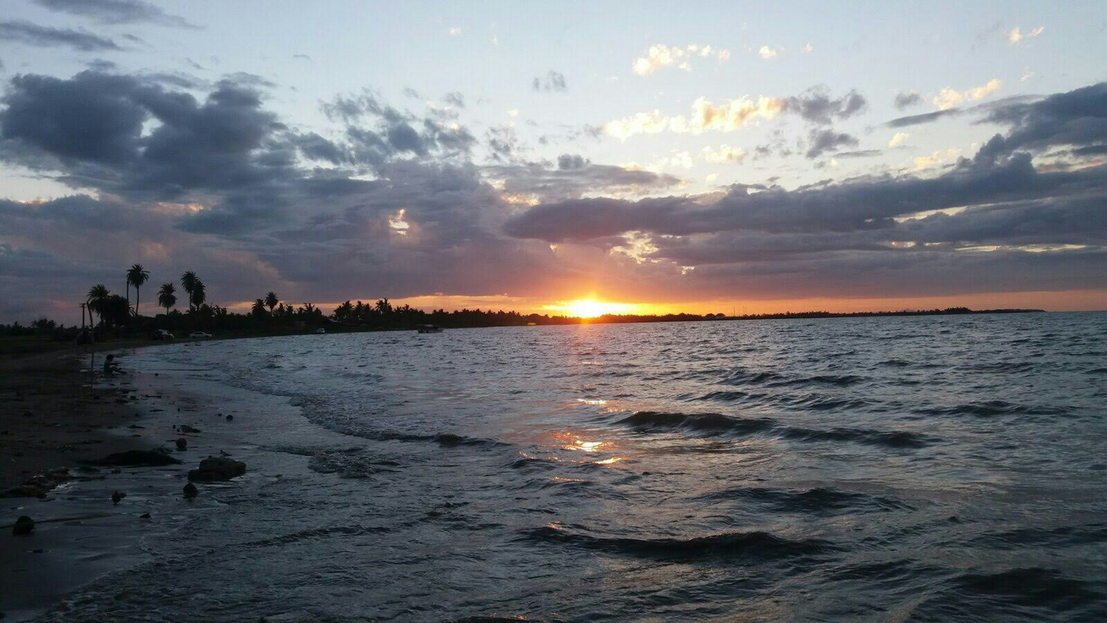 Sebuah matahari terbenam yang indah di atas laut dengan air berombak dan awan yang tersebar