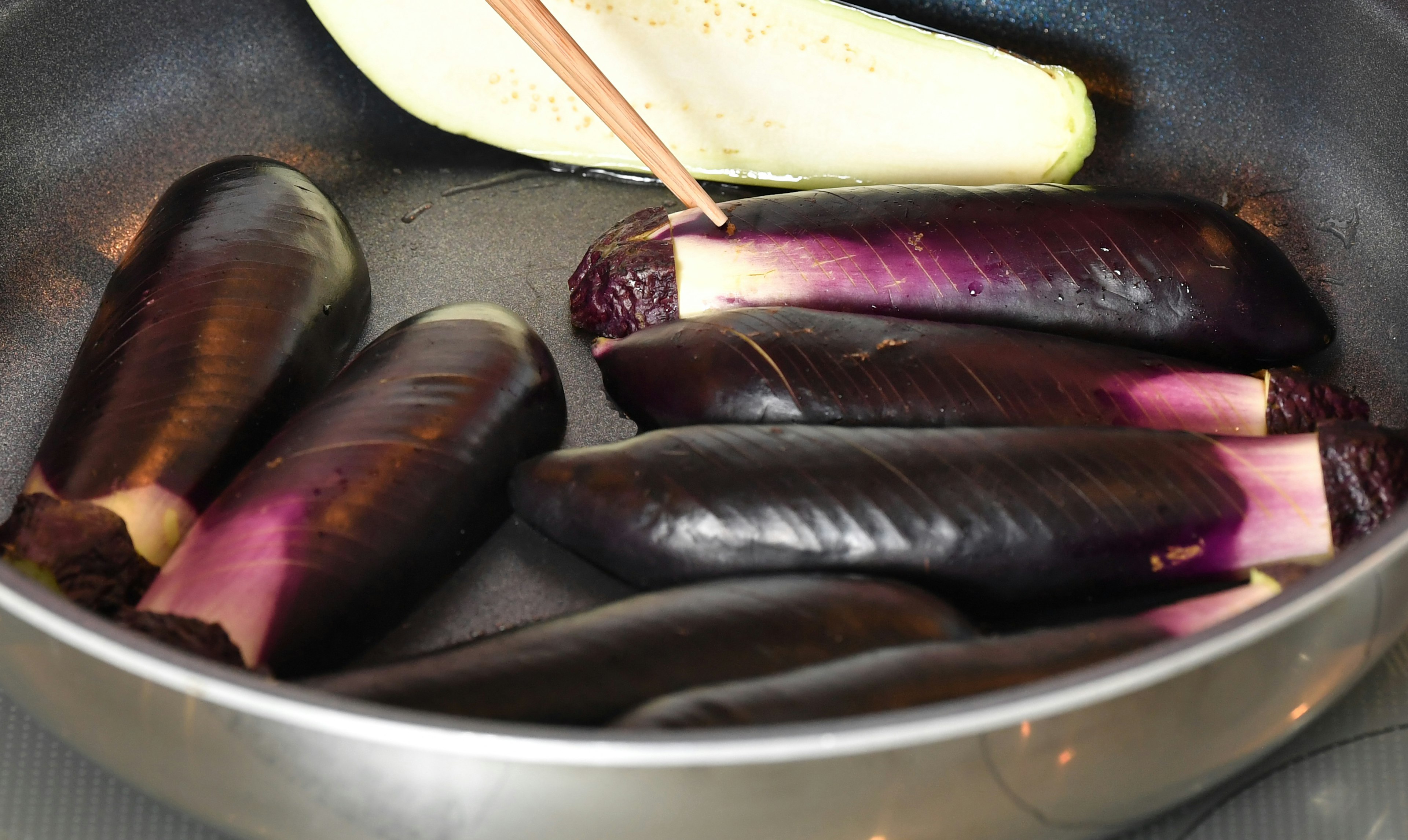 Purple eggplants and a white eggplant in a frying pan