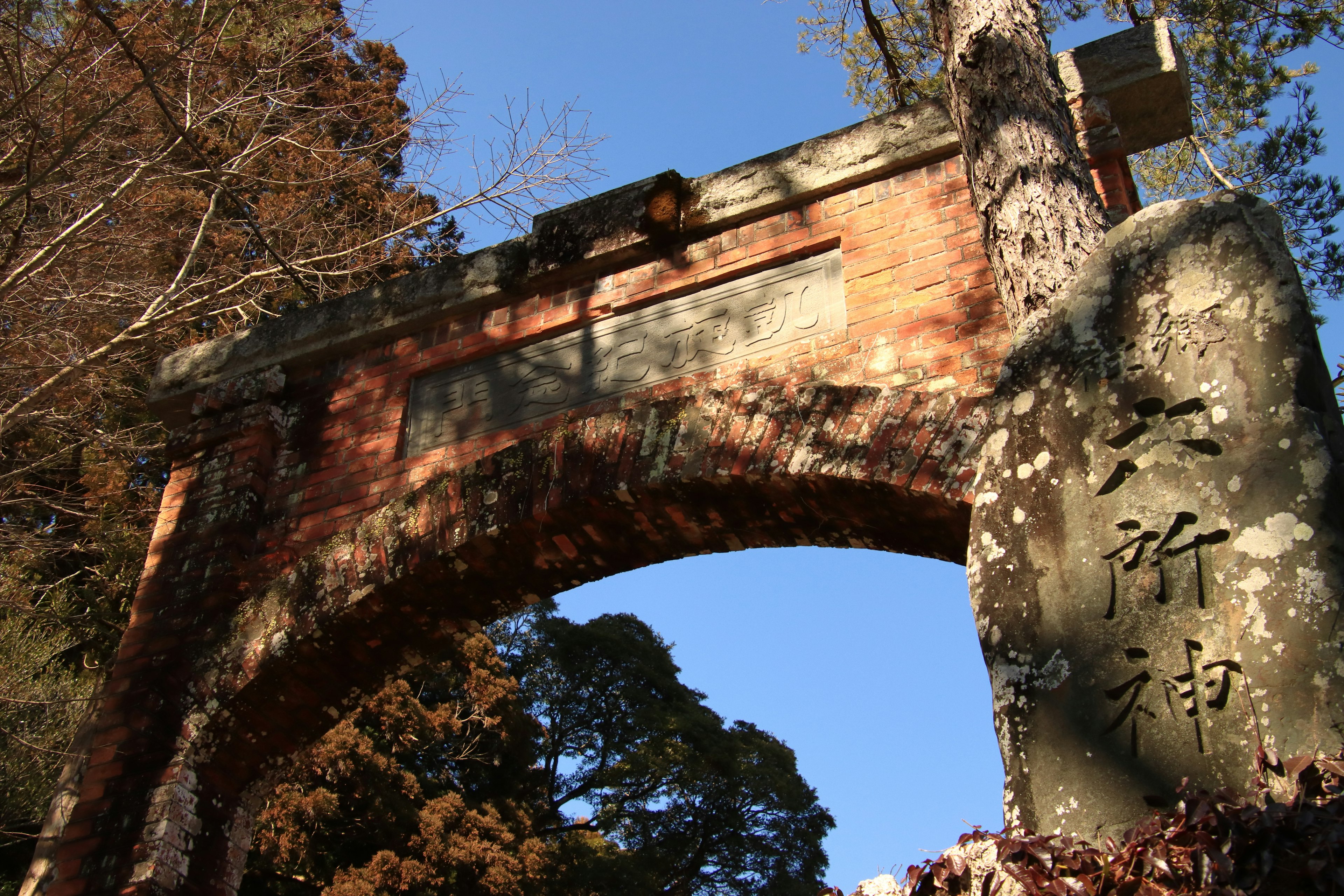 Une ancienne arche en briques avec un monument en pierre entouré d'arbres