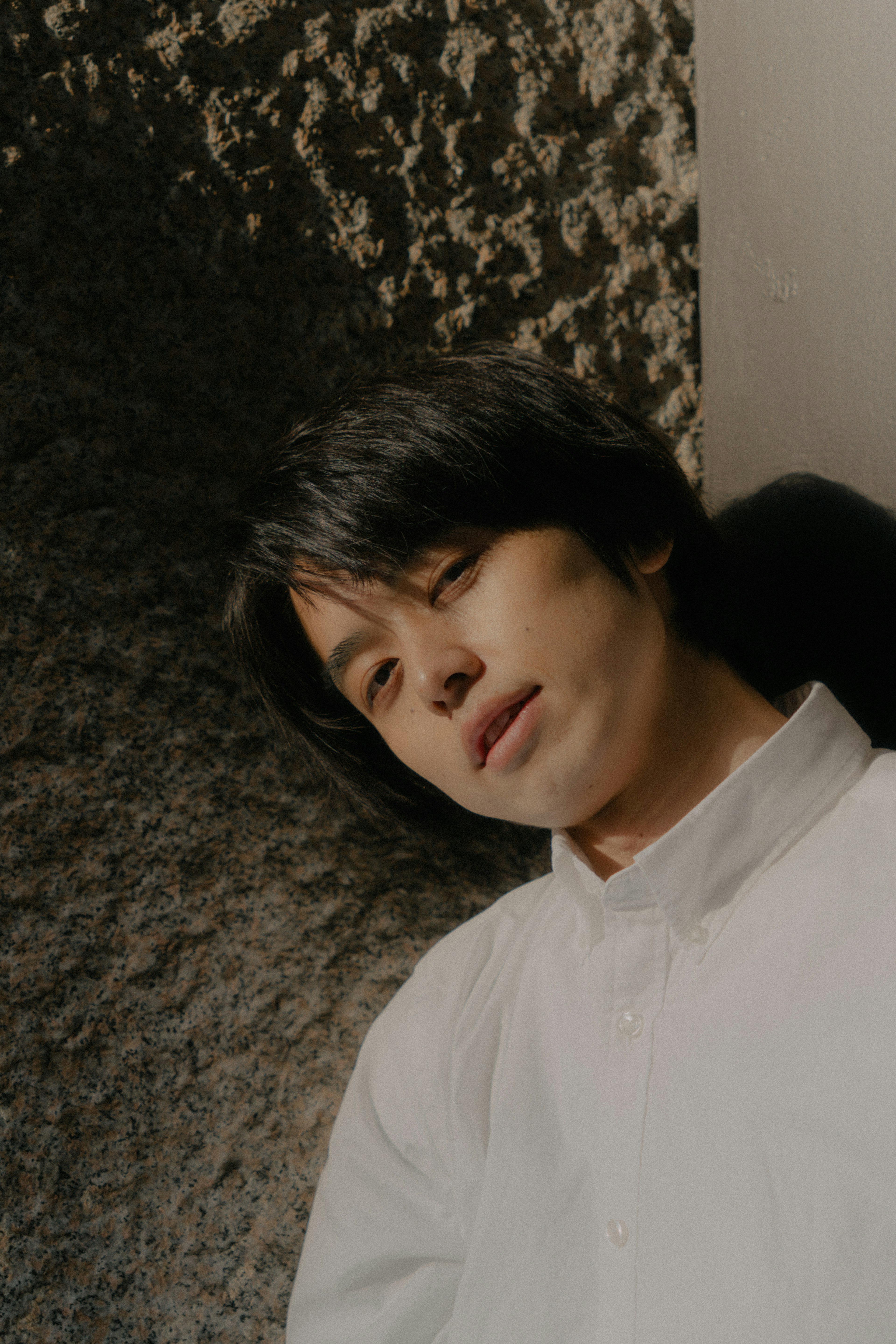 A young man leaning against a wall with a natural expression and soft lighting