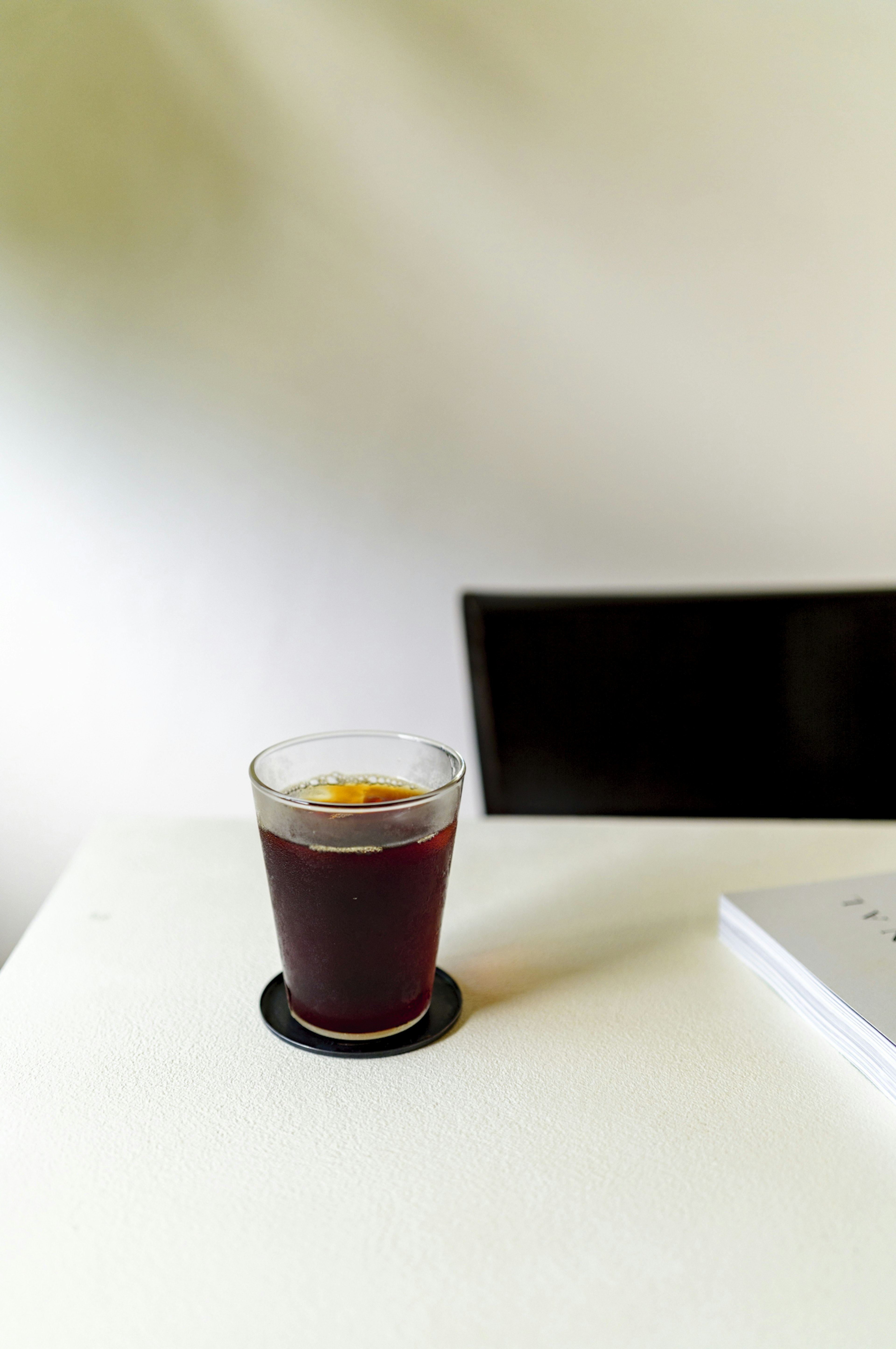 A glass of coffee on a table with a black device in the background