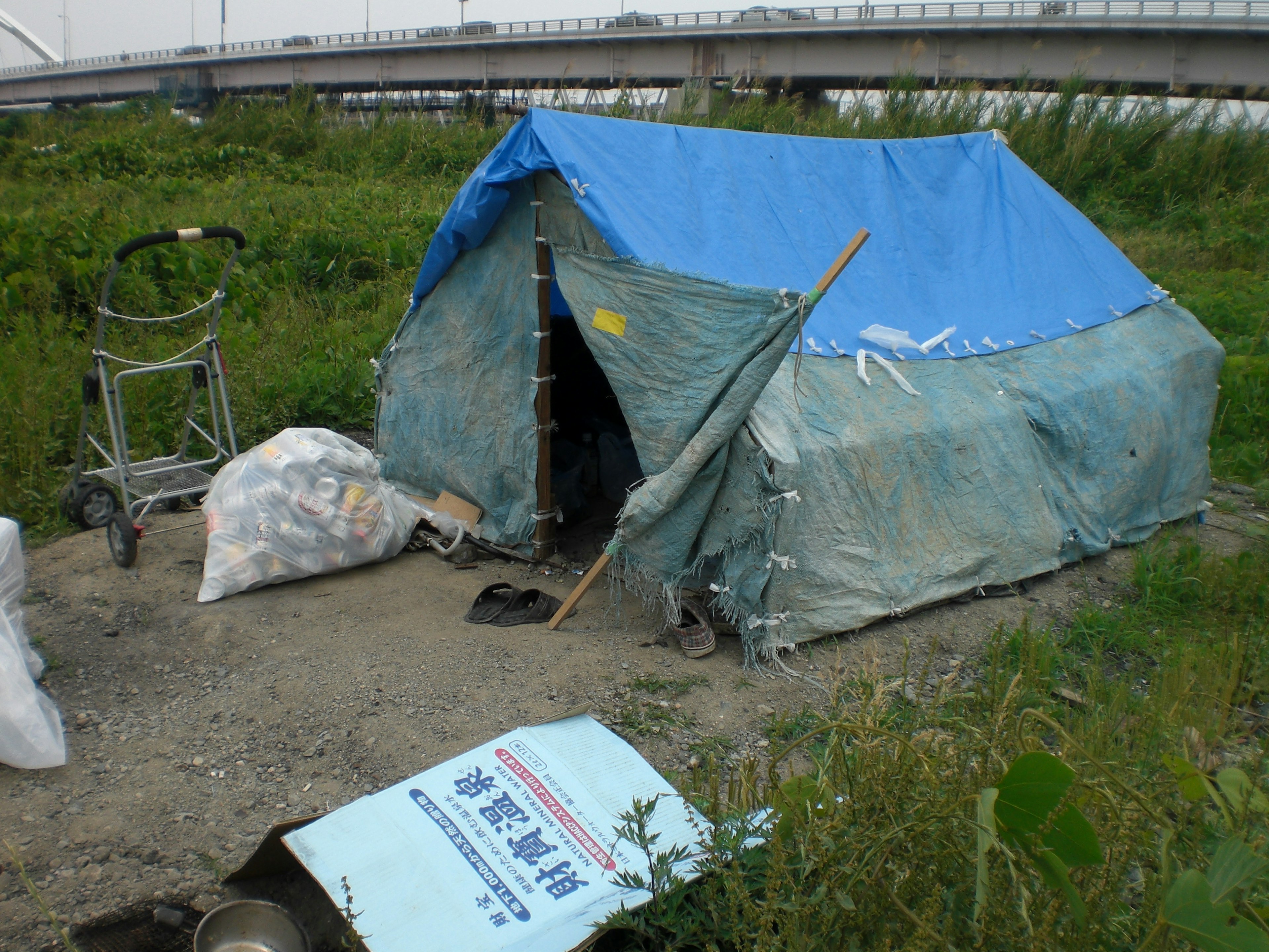 A makeshift tent with a blue tarp surrounded by garbage bags