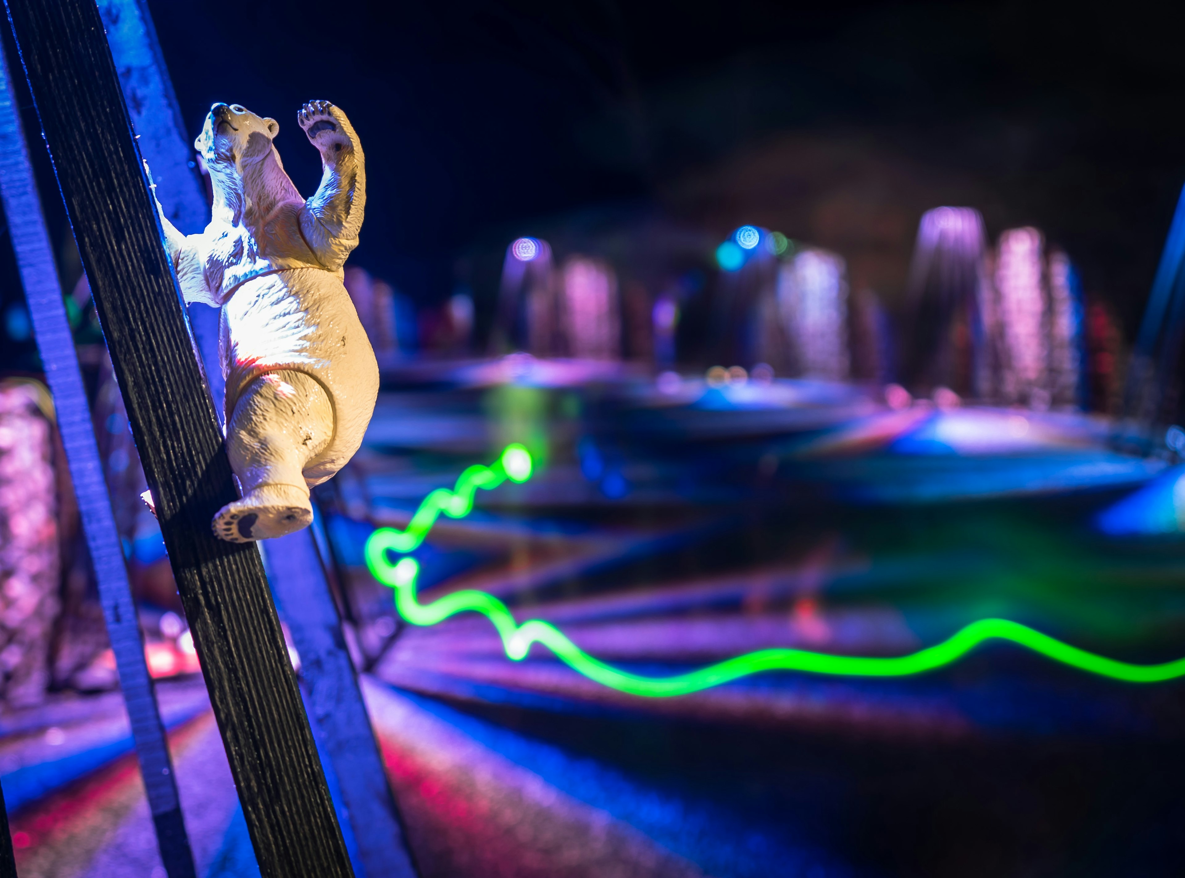 Eine weiße Bärenfigur, die einen Holzpfosten in einer dunklen Umgebung erklimmt Bunte Lichtstrahlen beleuchten die Umgebung