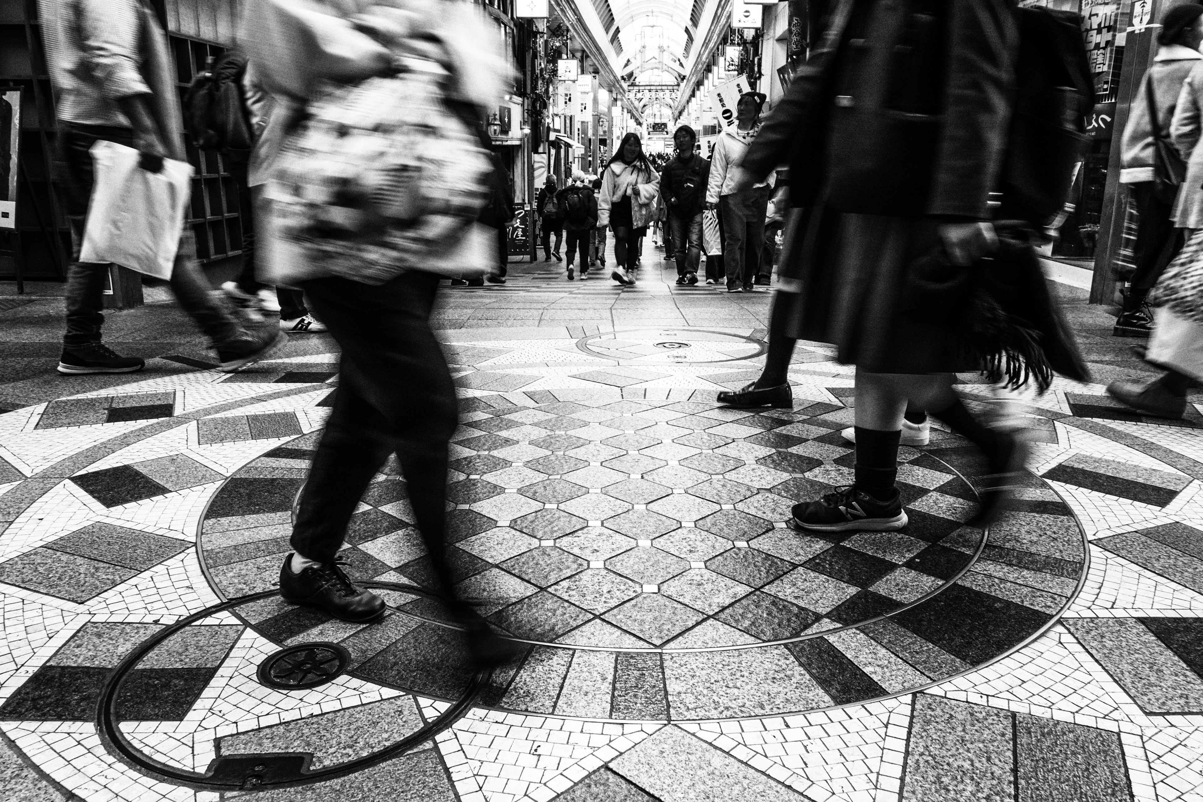 Imagen en blanco y negro de personas caminando en una galería comercial con un suelo de mosaico intrincado