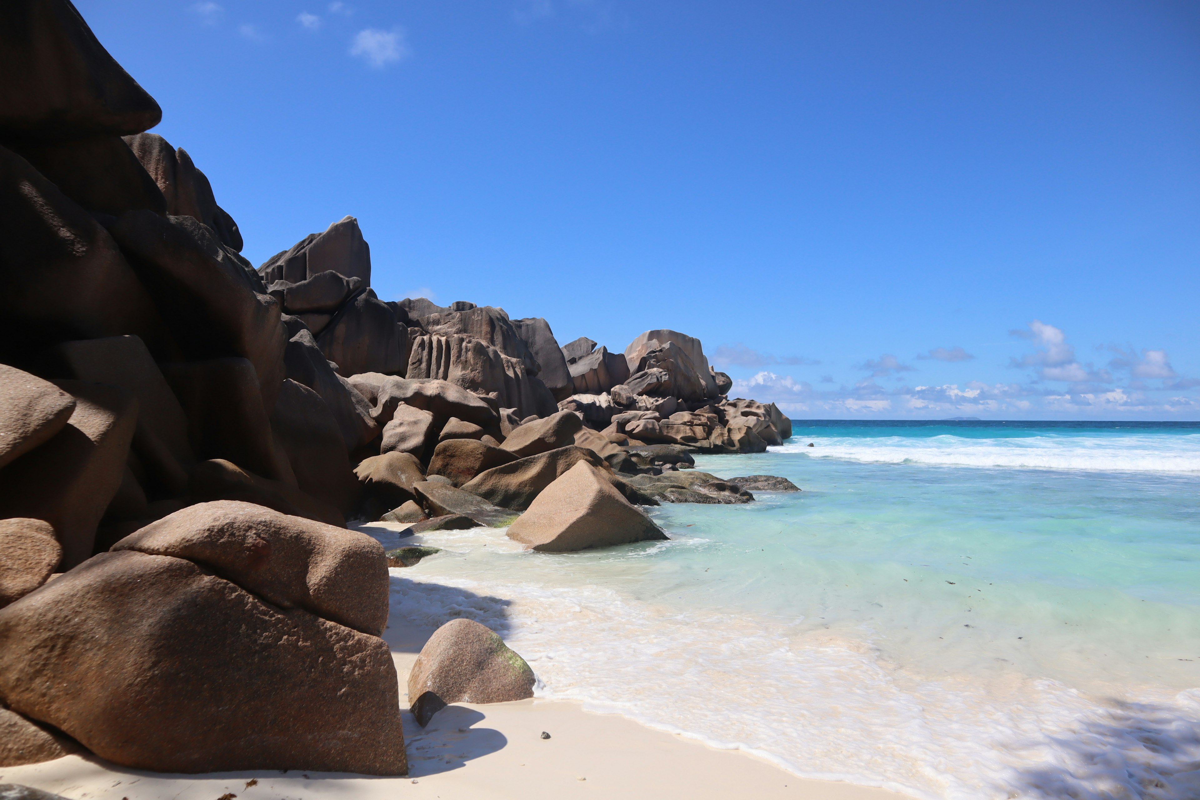 ชายหาดที่มีหินใหญ่ล้อมรอบด้วยทะเลสีน้ำเงินและทรายขาว