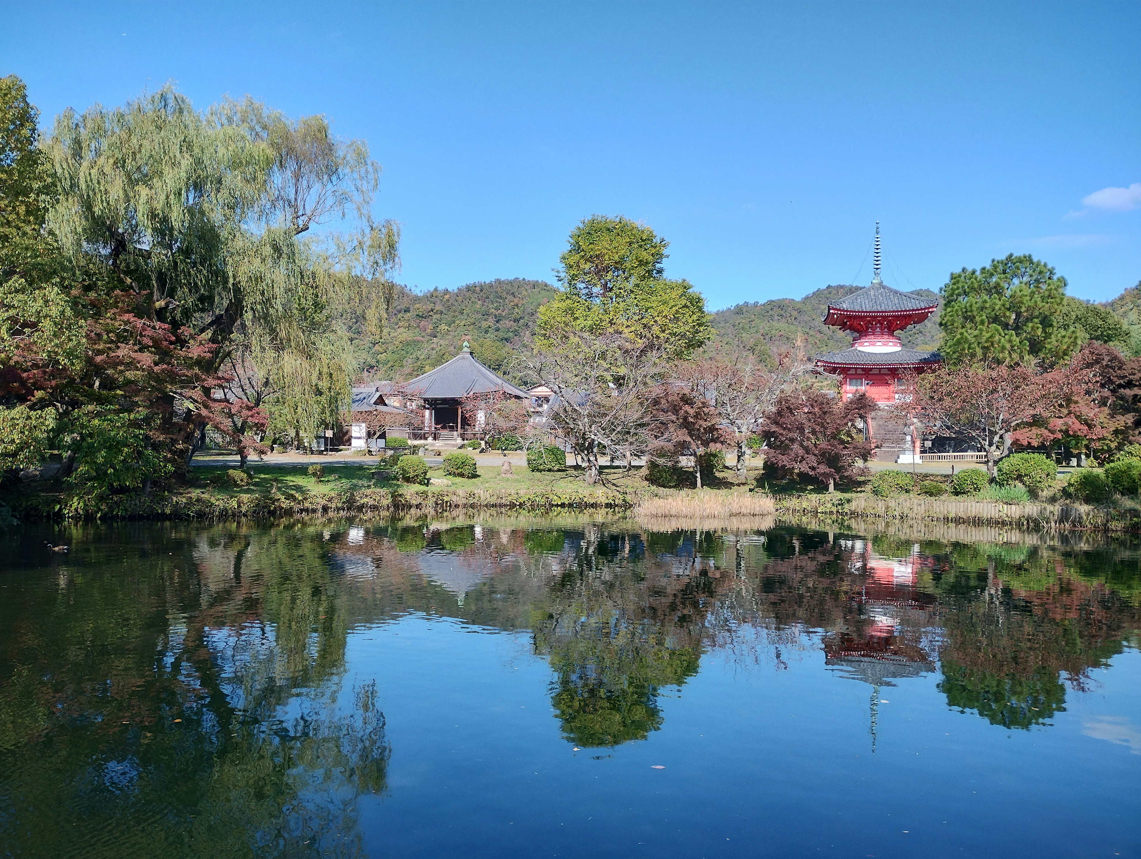 Traditional Japanese buildings and a red pagoda reflected in a serene pond