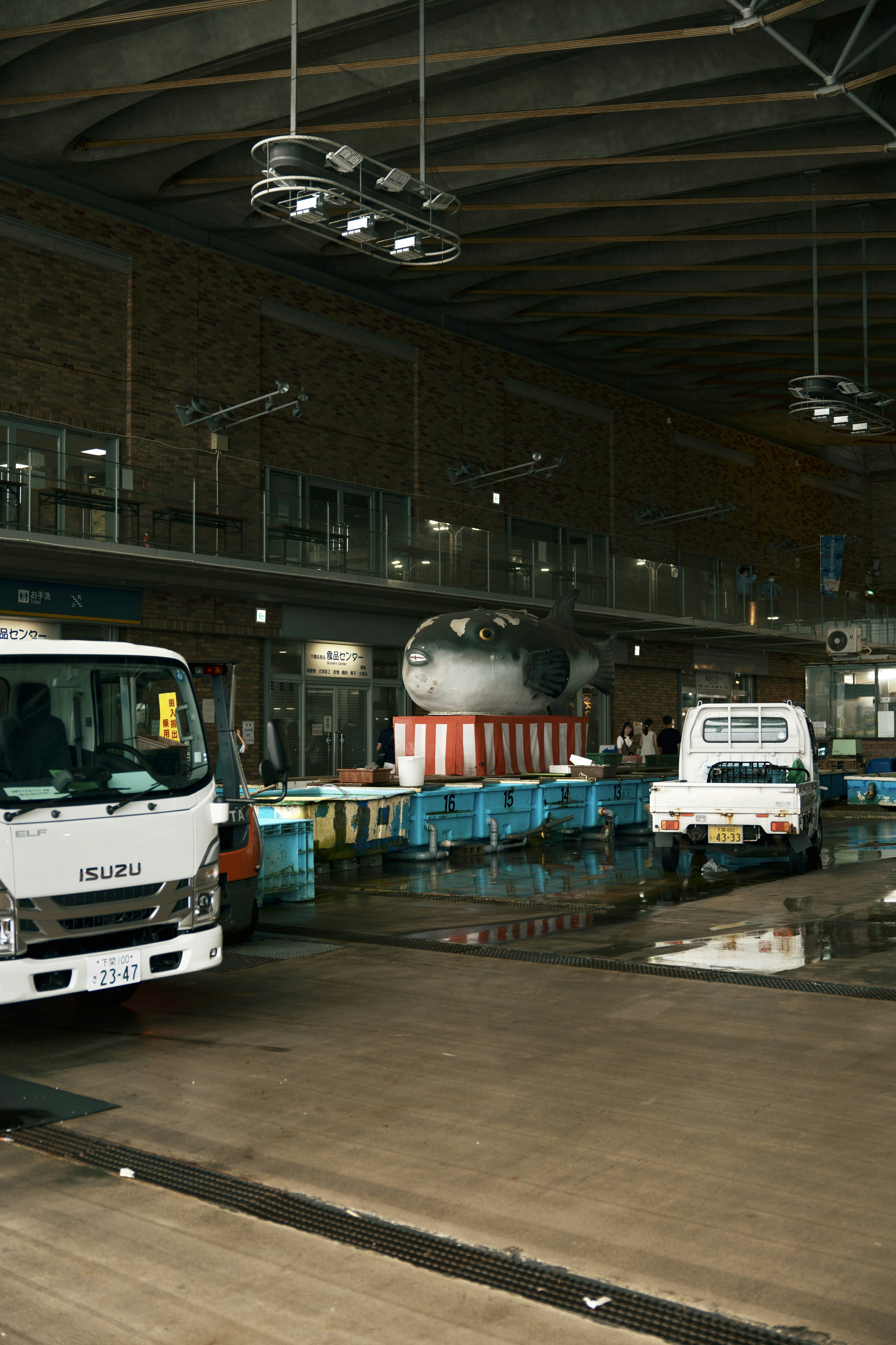 Intérieur d'un marché avec des camions et des caisses bleues alignées présentant un grand poisson au centre