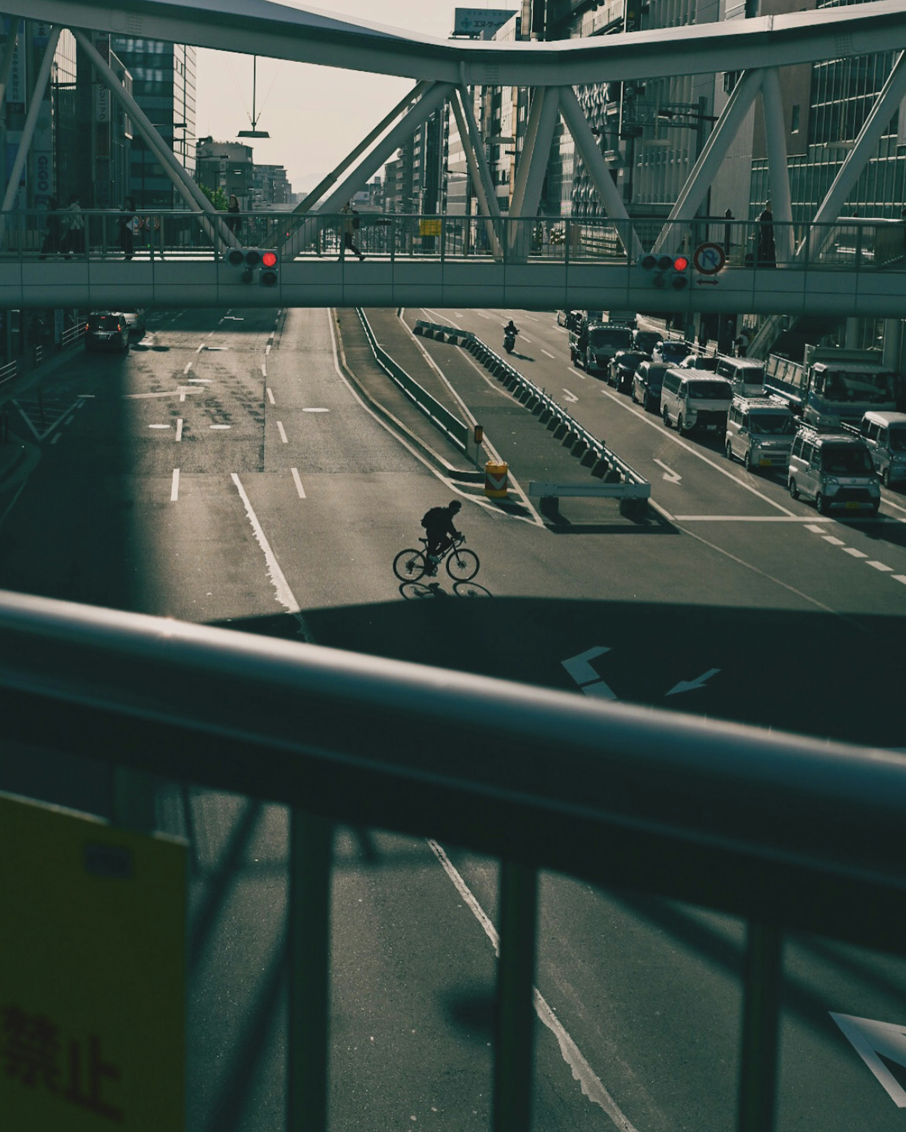 Urban street scene with a cyclist on the road and an overhead pedestrian bridge