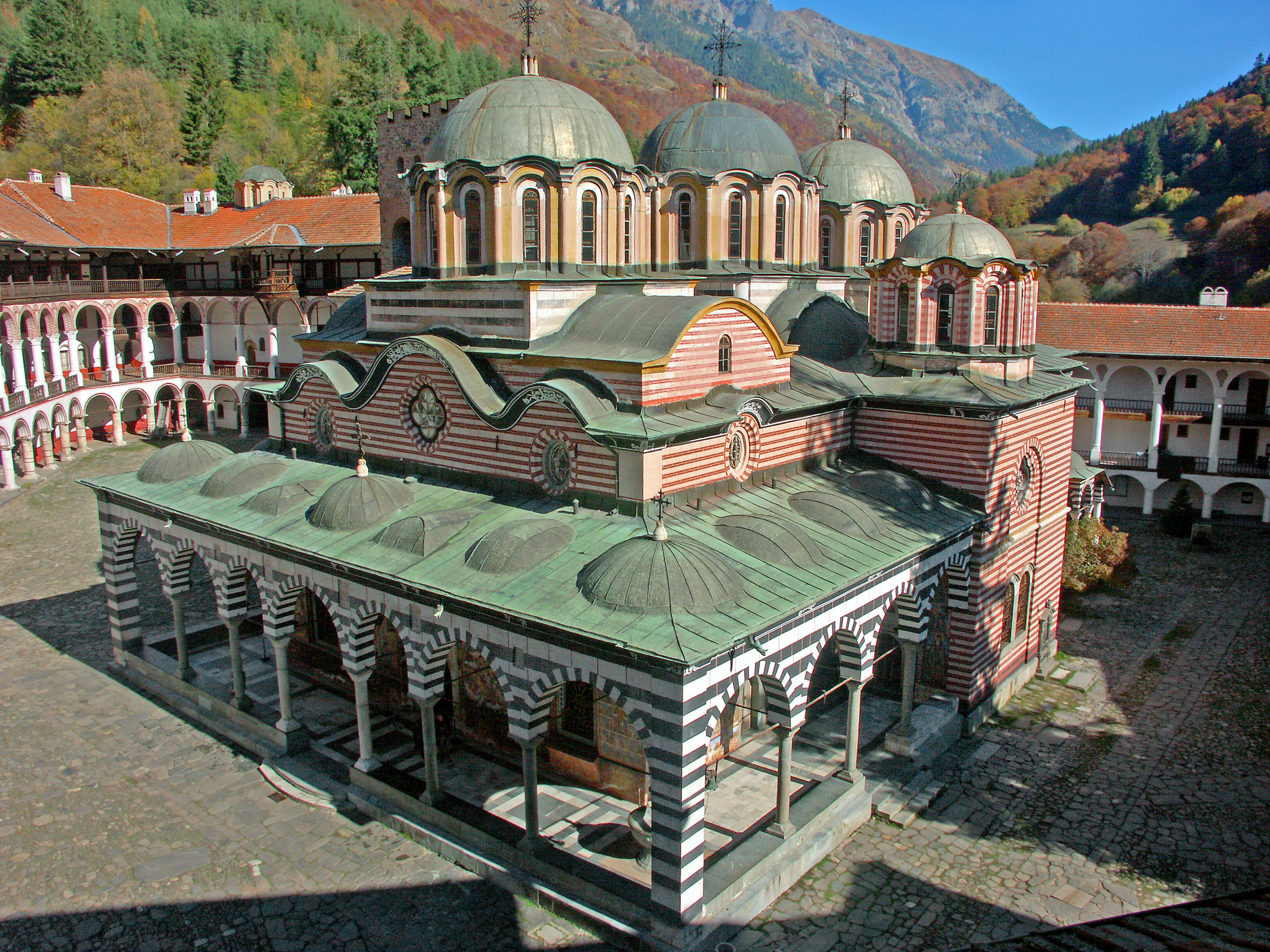 A picturesque monastery building with domes surrounded by autumn foliage