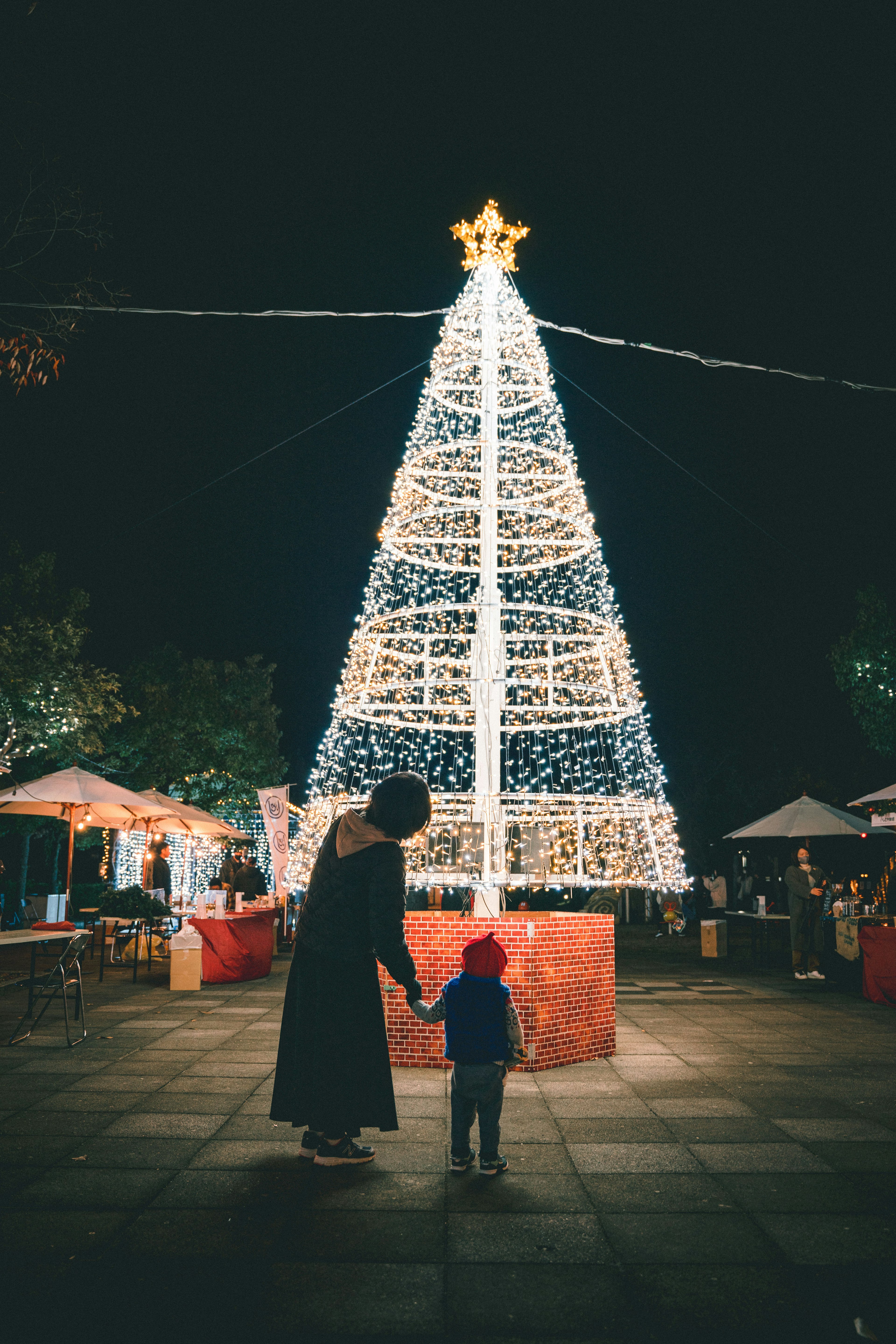 Silhouette eines Elternteils und eines Kindes vor einem beleuchteten Weihnachtsbaum bei Nacht