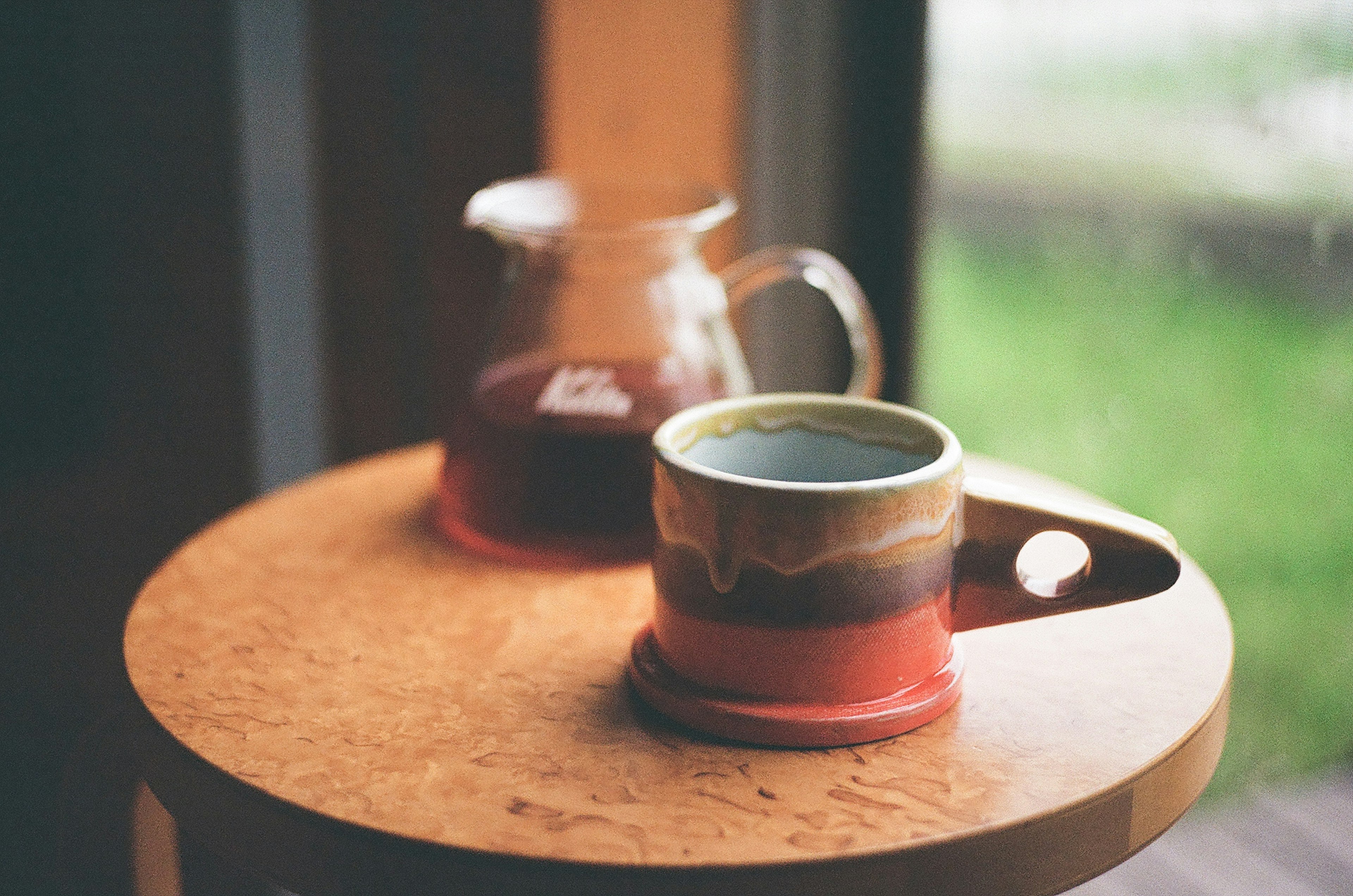 Taza de café y tetera sobre una mesa de madera con luz natural