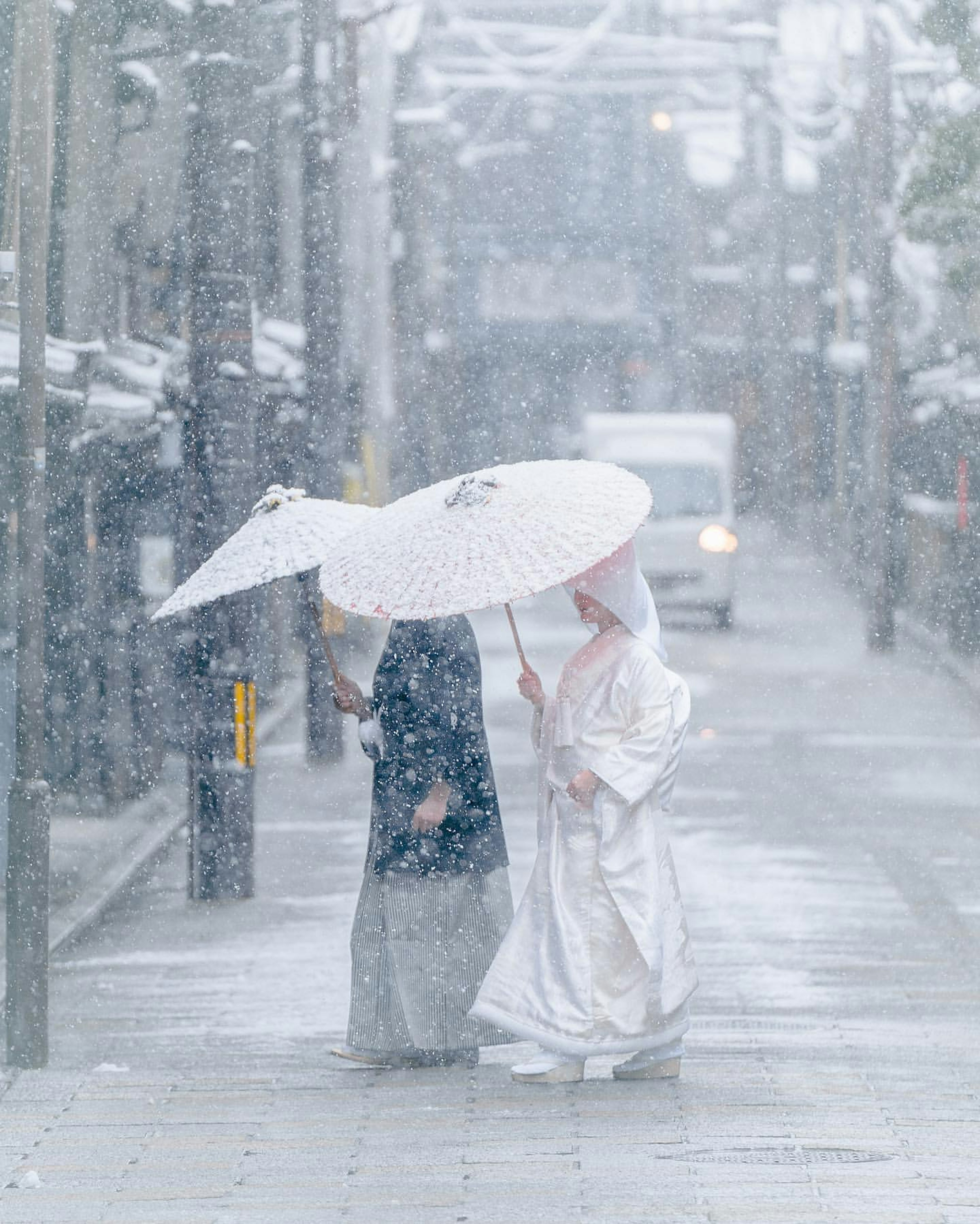 Frauen in traditioneller Kleidung, die im Schnee unter Regenschirmen gehen