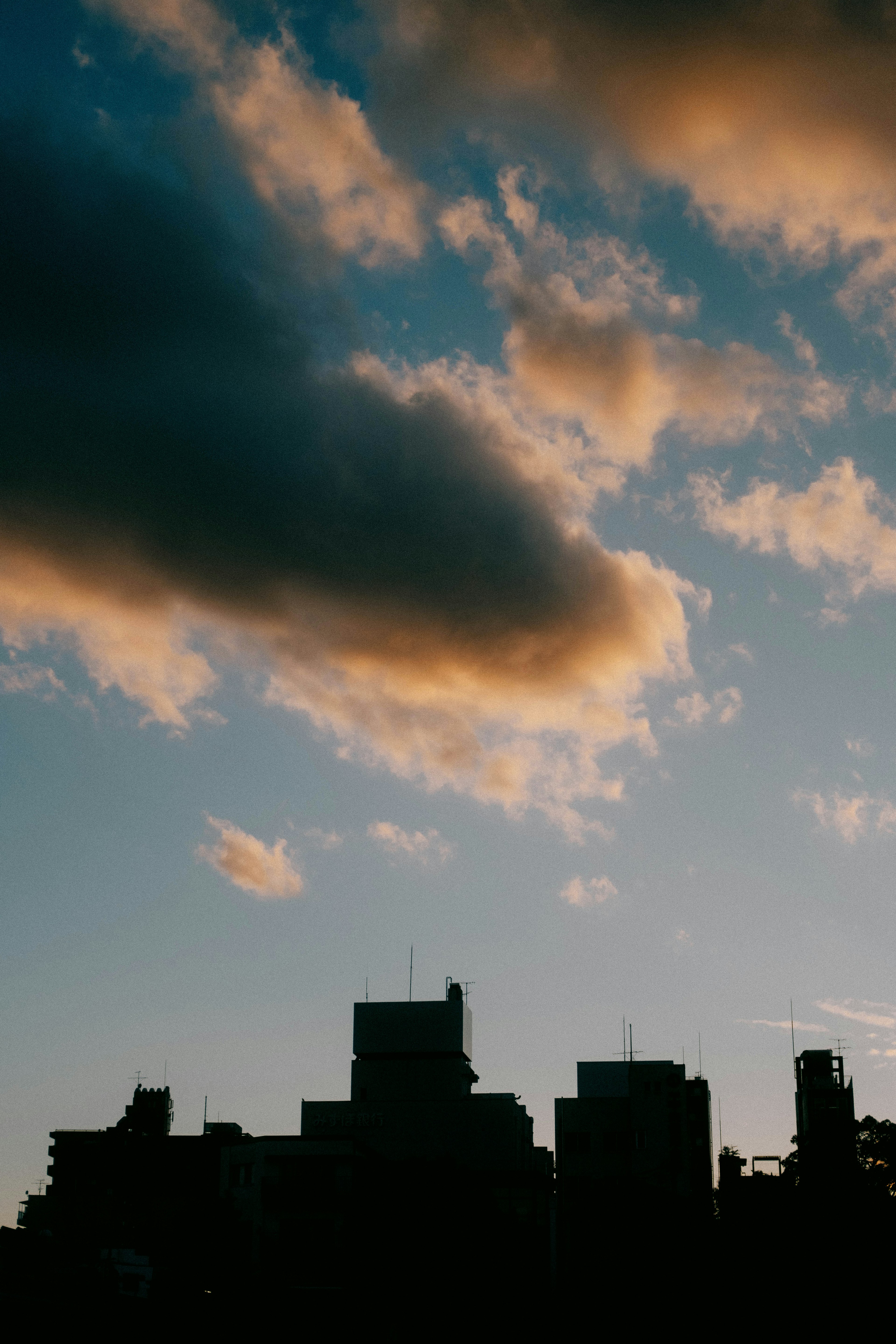 Silueta de un horizonte urbano contra un cielo azul con nubes al atardecer