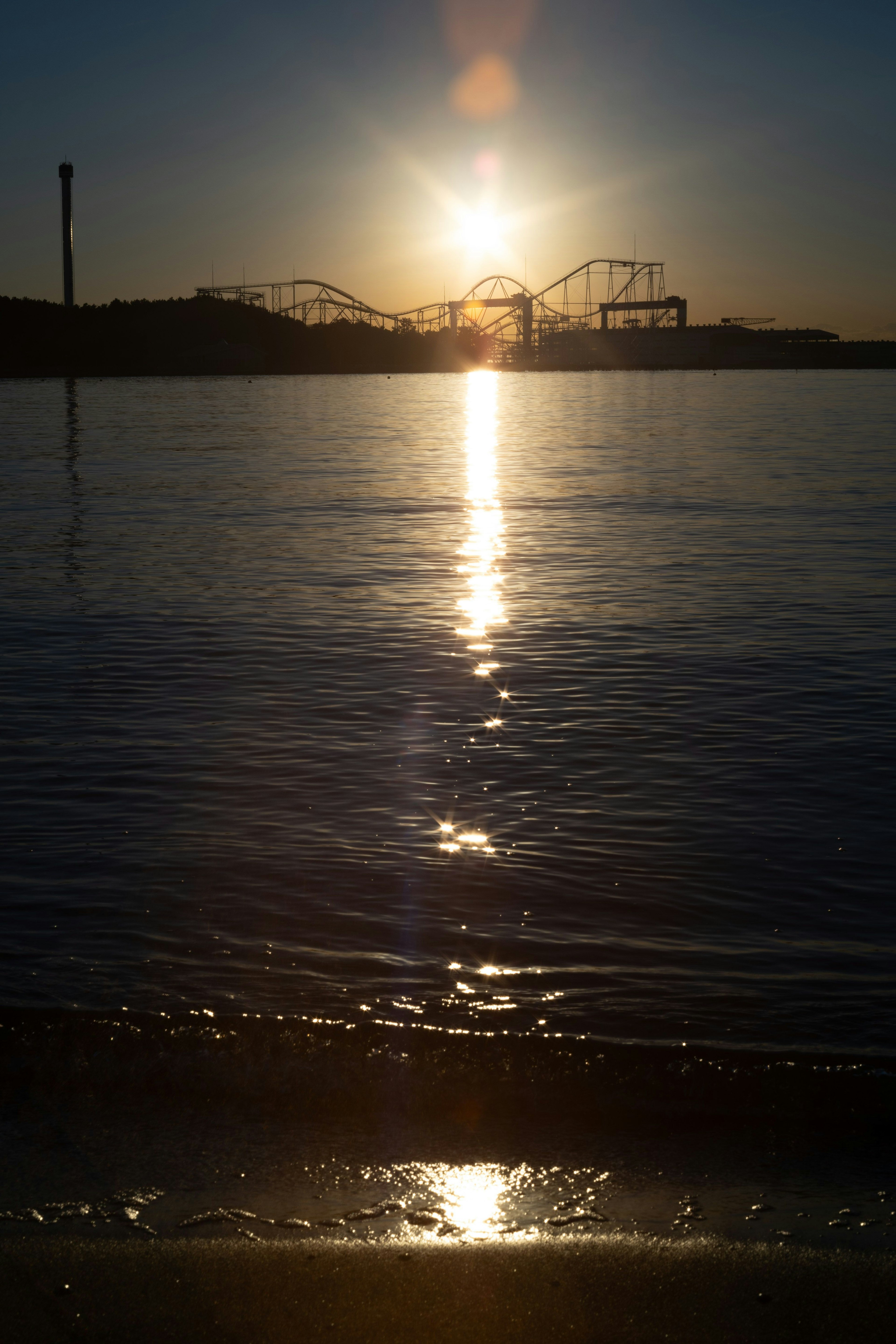 夕日が水面に反射する海の景色 遠くに遊園地のシルエット