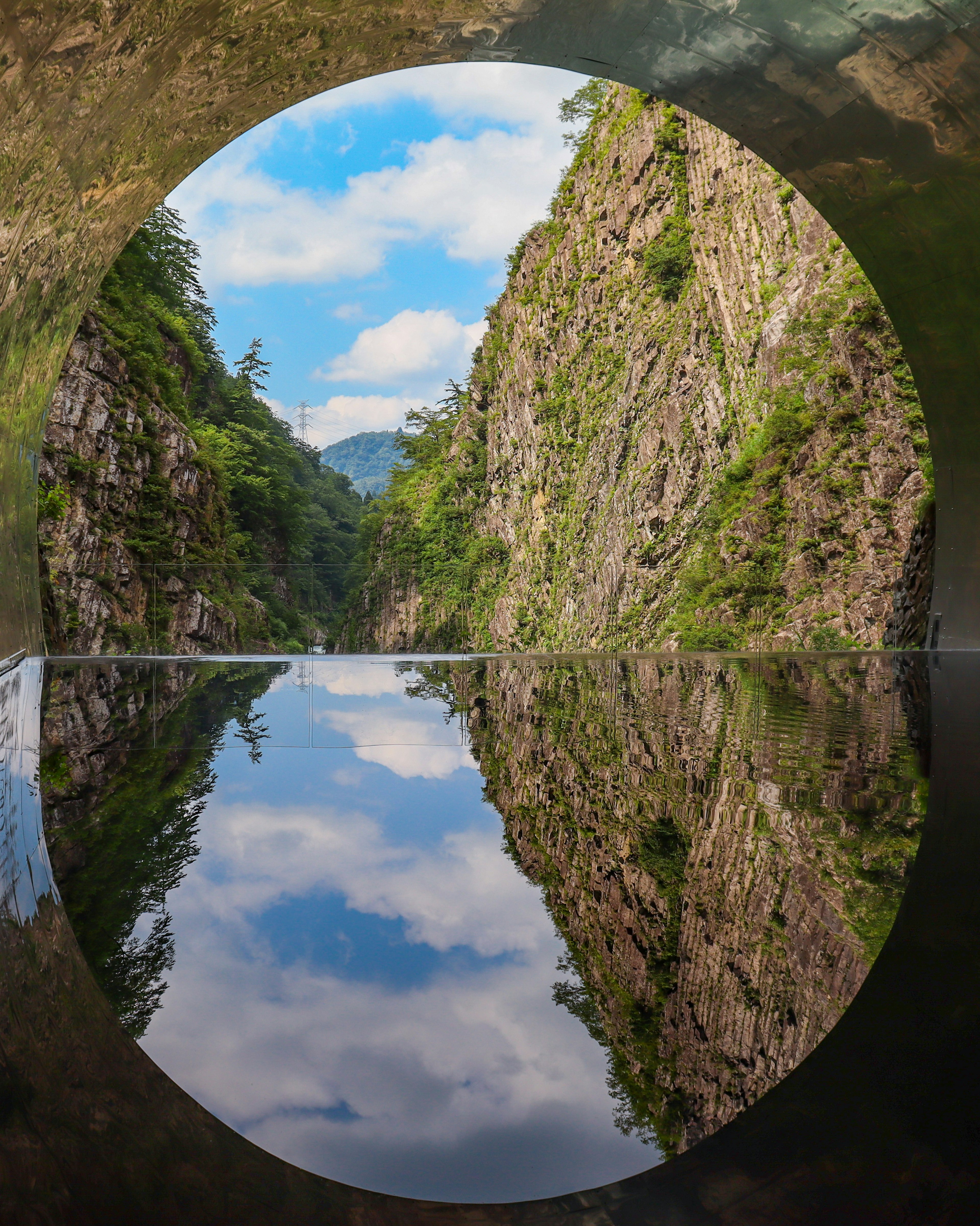 Circular frame revealing lush cliffs and sky reflection