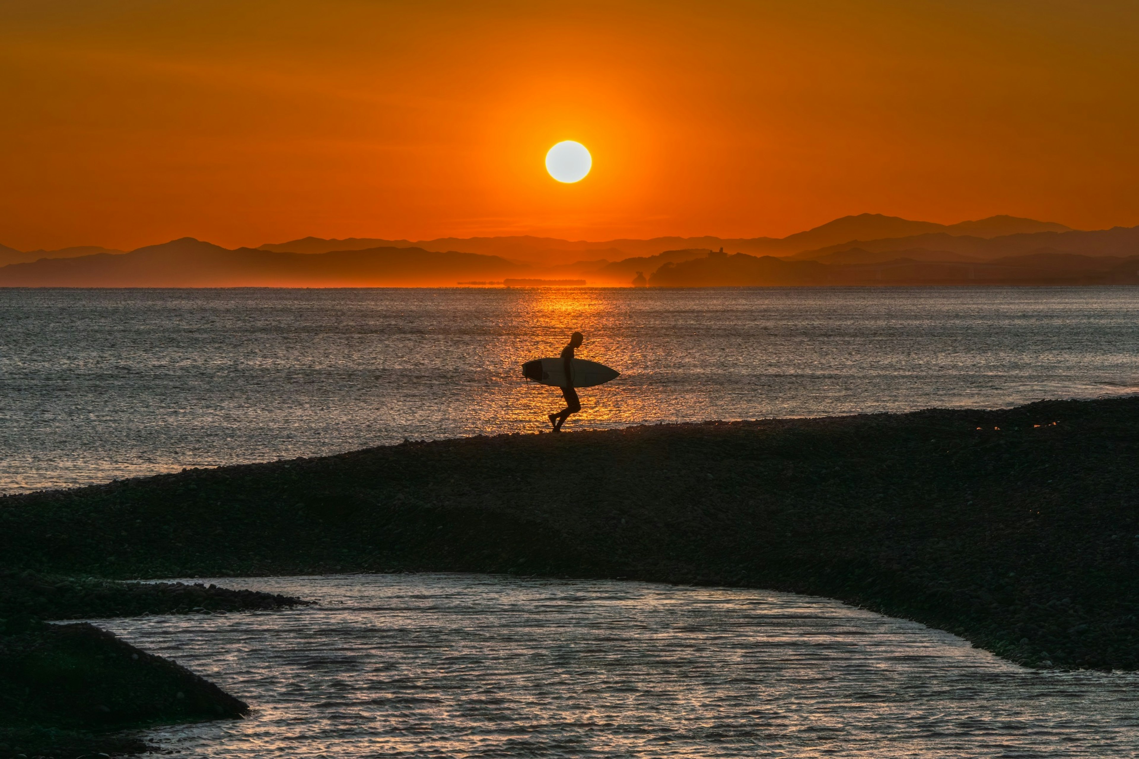 Silhouette of a surfer against a sunset Ocean view with gentle waves