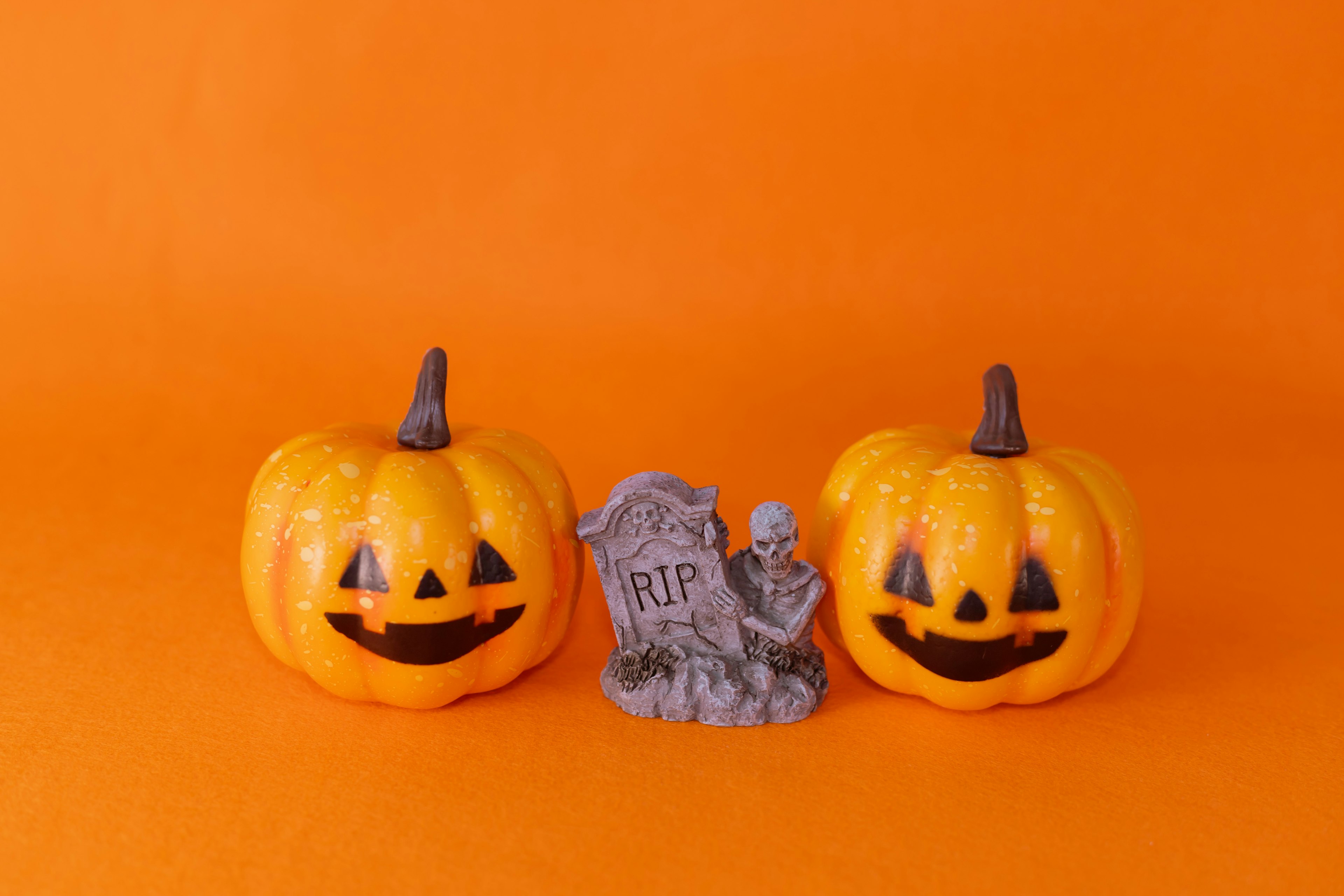 Two smiling jack-o'-lanterns and a tombstone decoration on an orange background