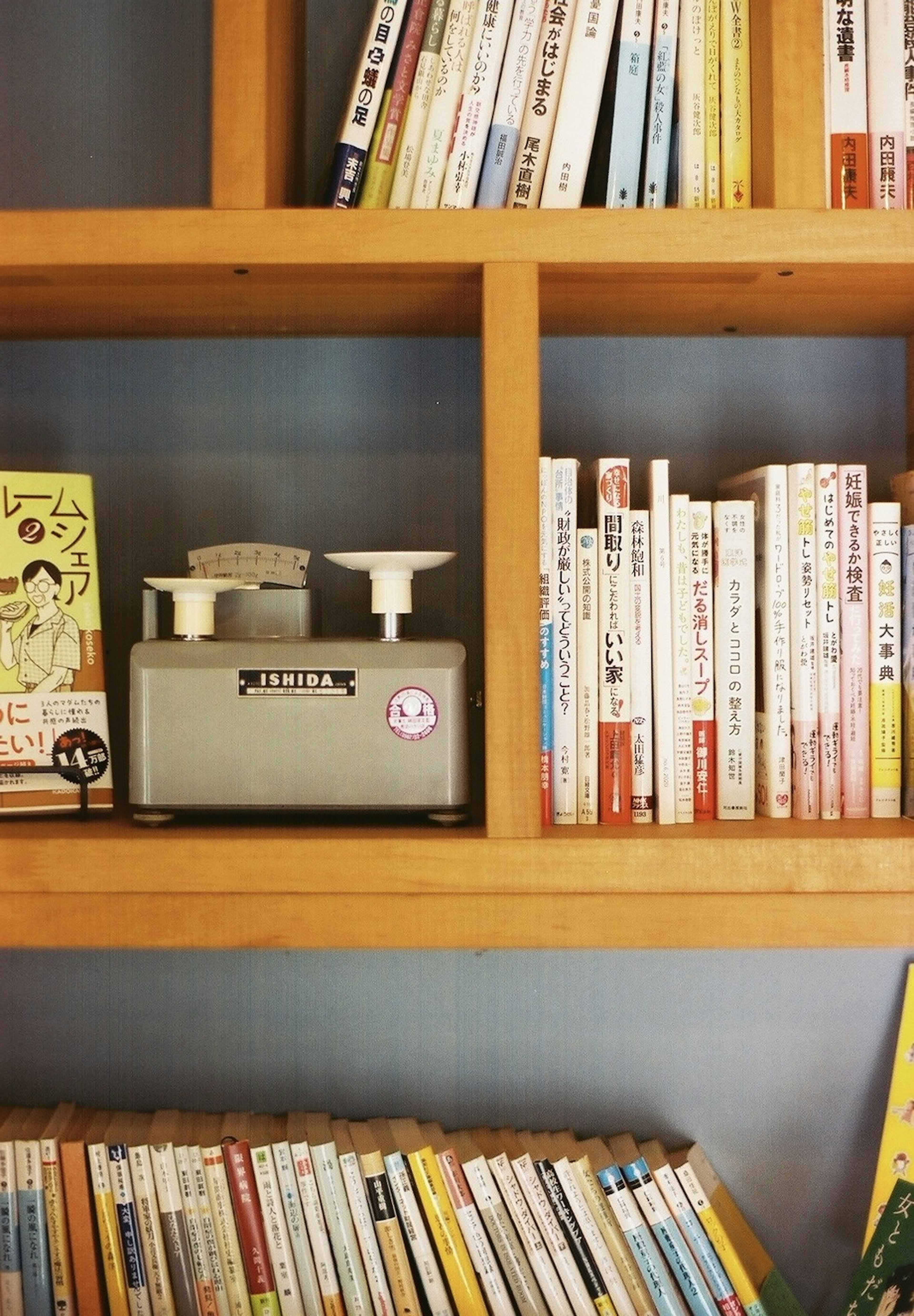 A wooden bookshelf filled with books and a gray scale placed on it