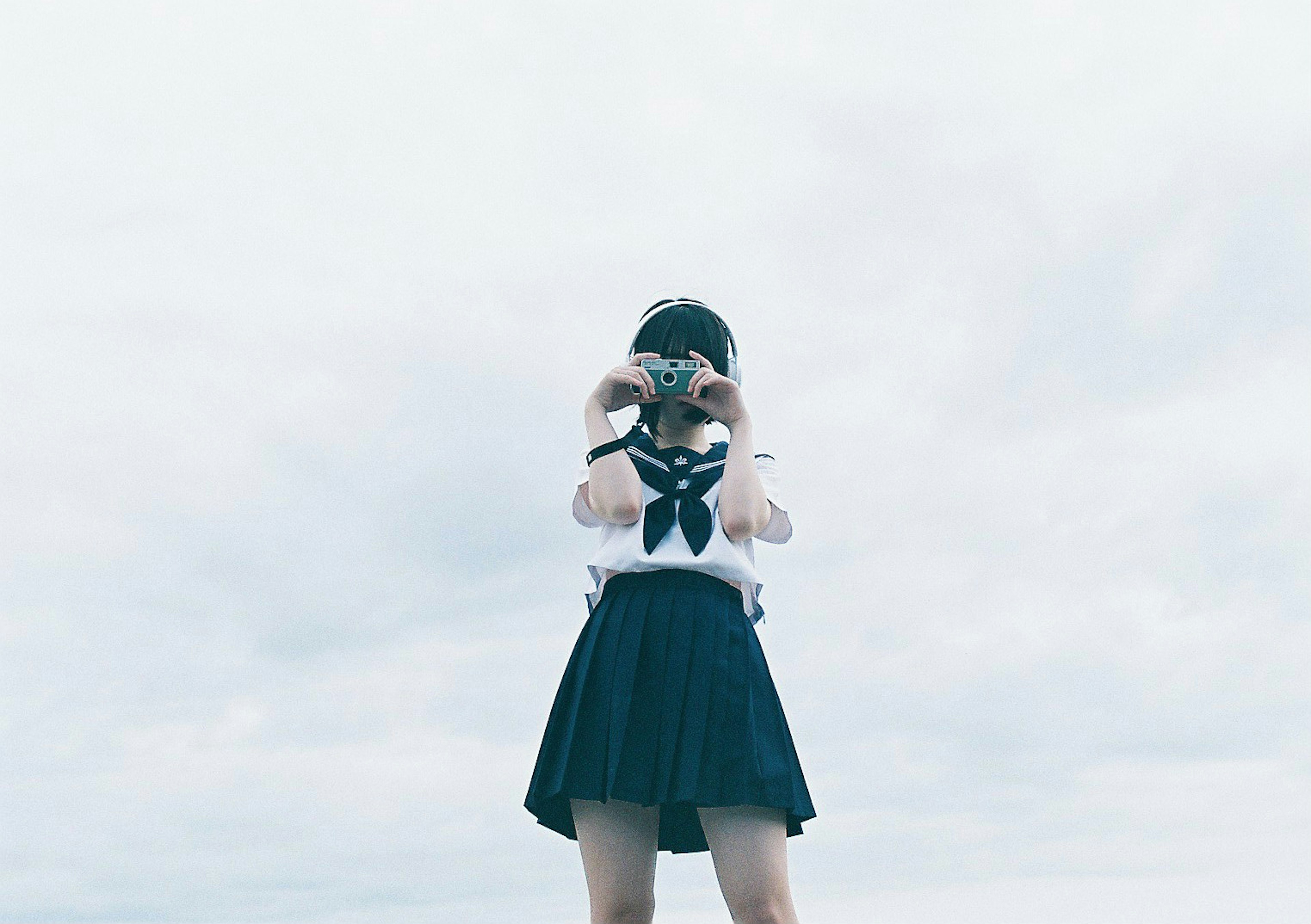 Ragazza che tiene una macchina fotografica indossando una camicia bianca e una gonna blu sotto un cielo nuvoloso