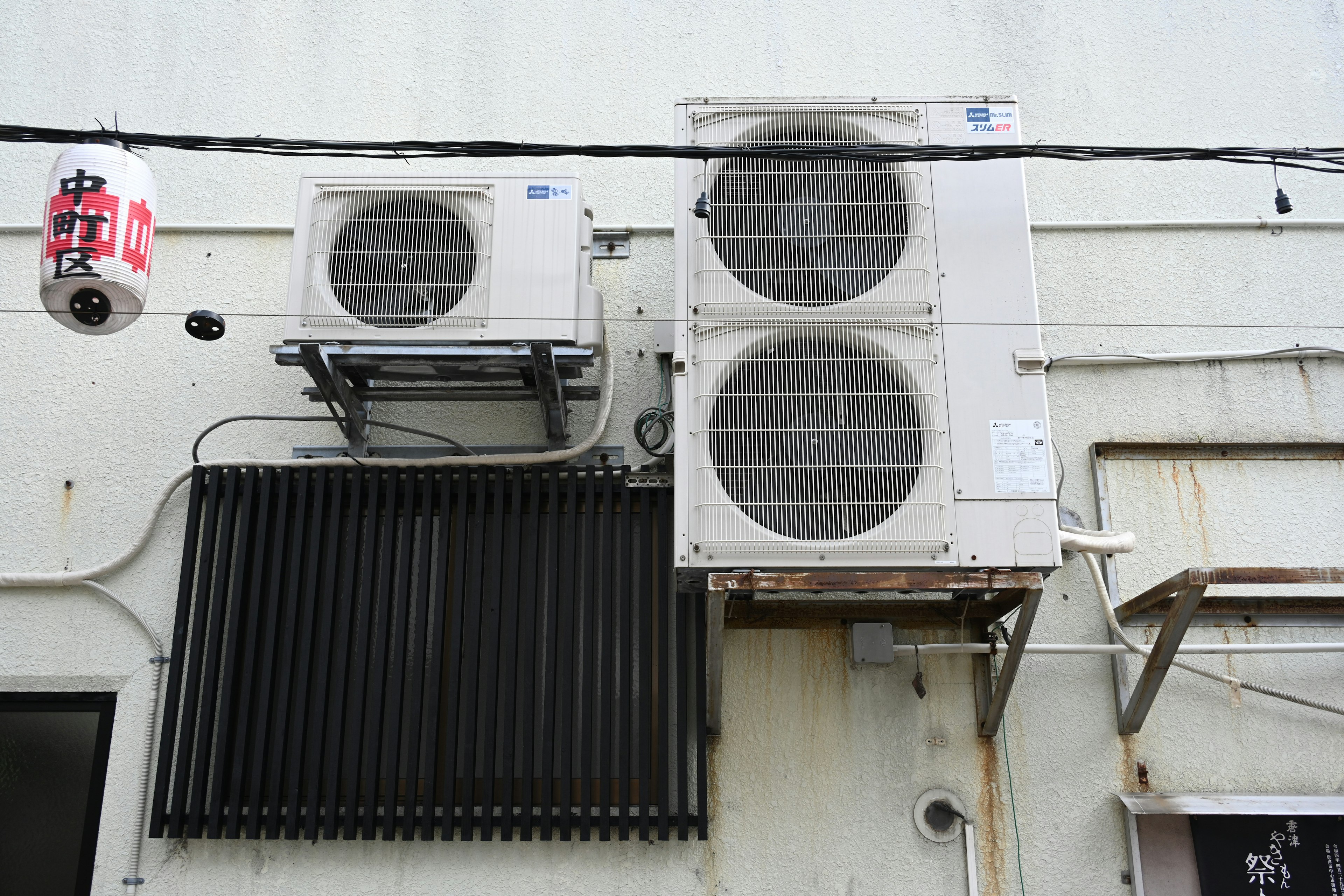 Two air conditioning units mounted on a wall with a black grill