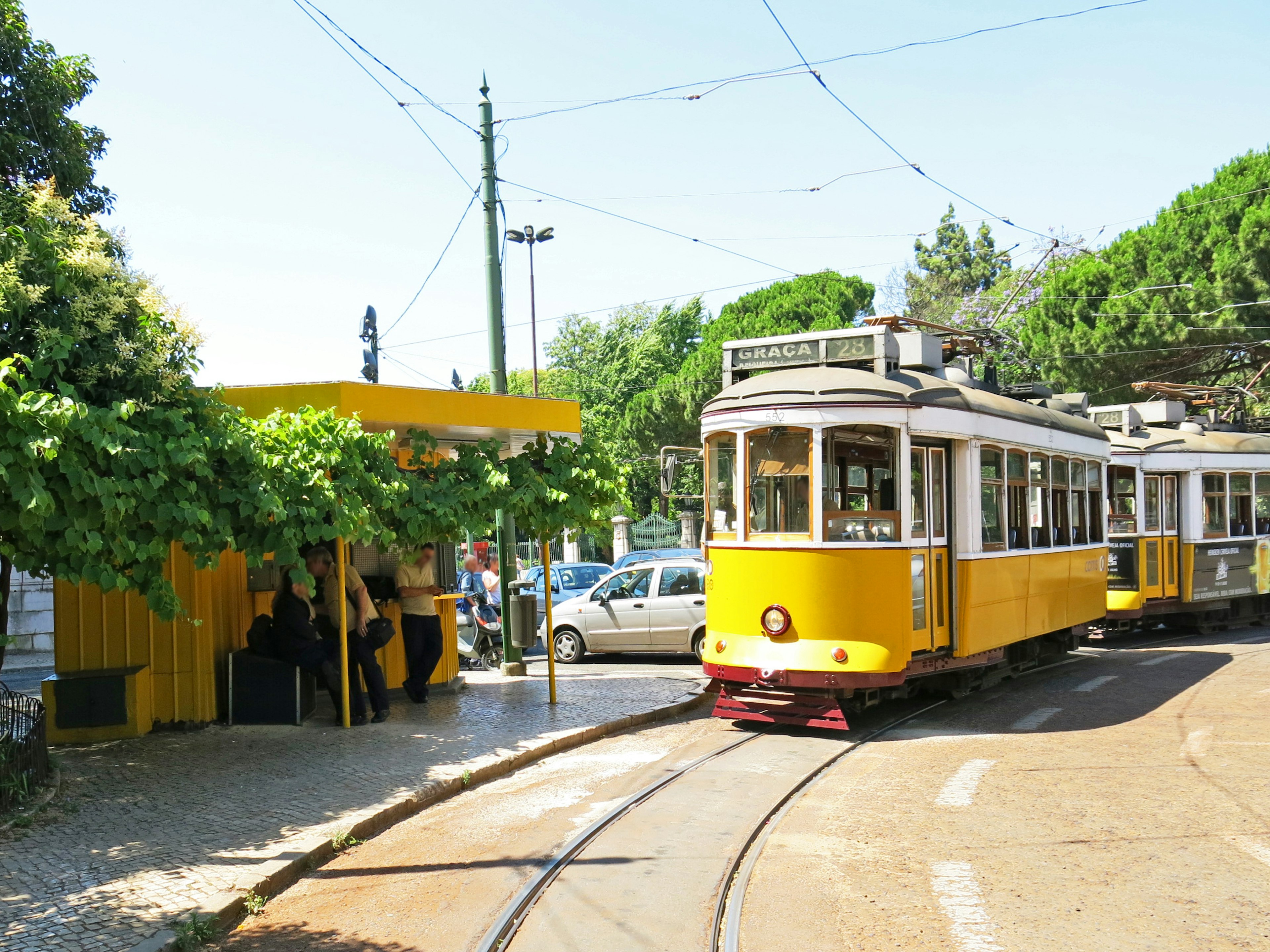 Yellow tram at a stop with surrounding greenery