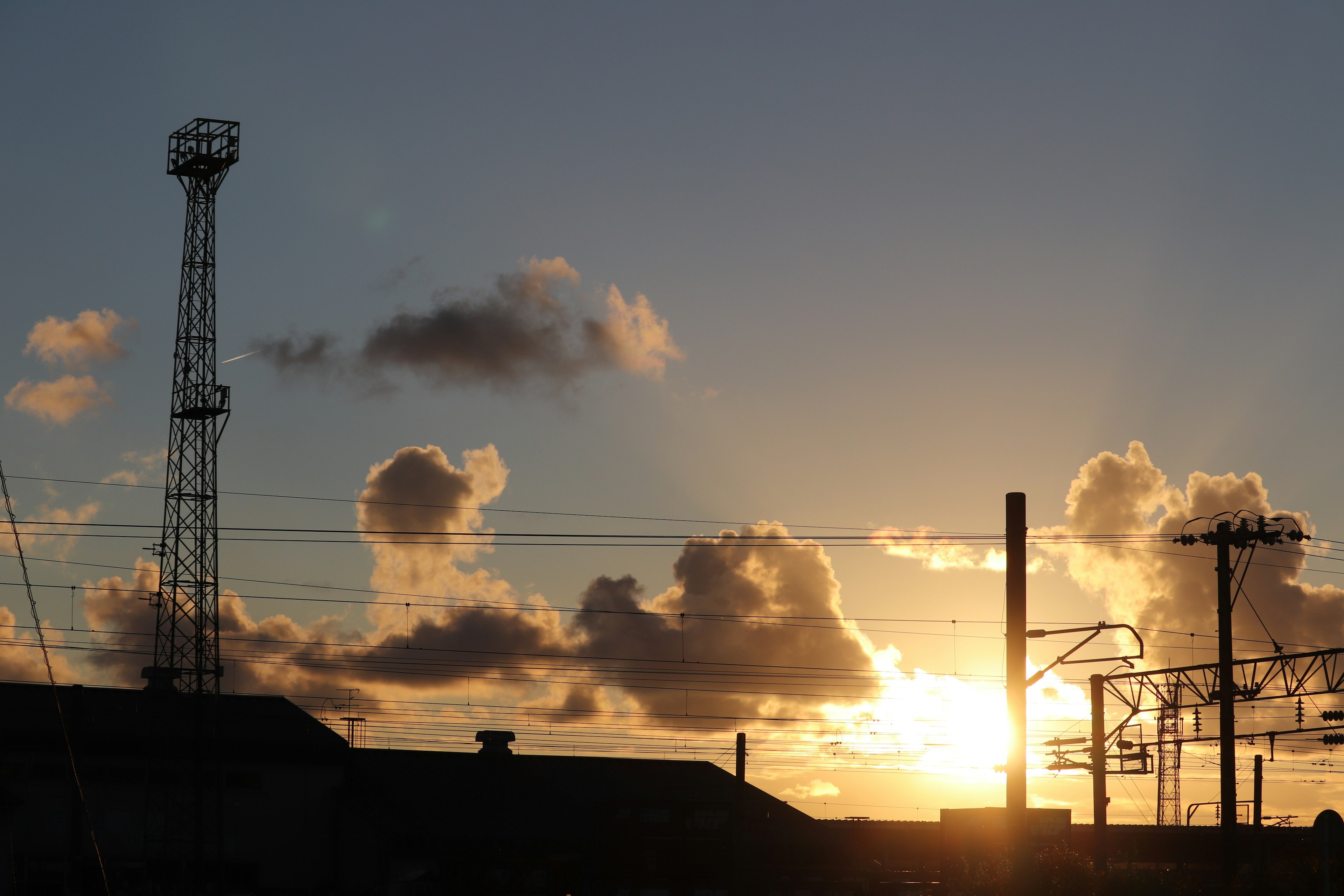 Silhouette di un'area industriale con un tramonto sullo sfondo che presenta torri alte e camini