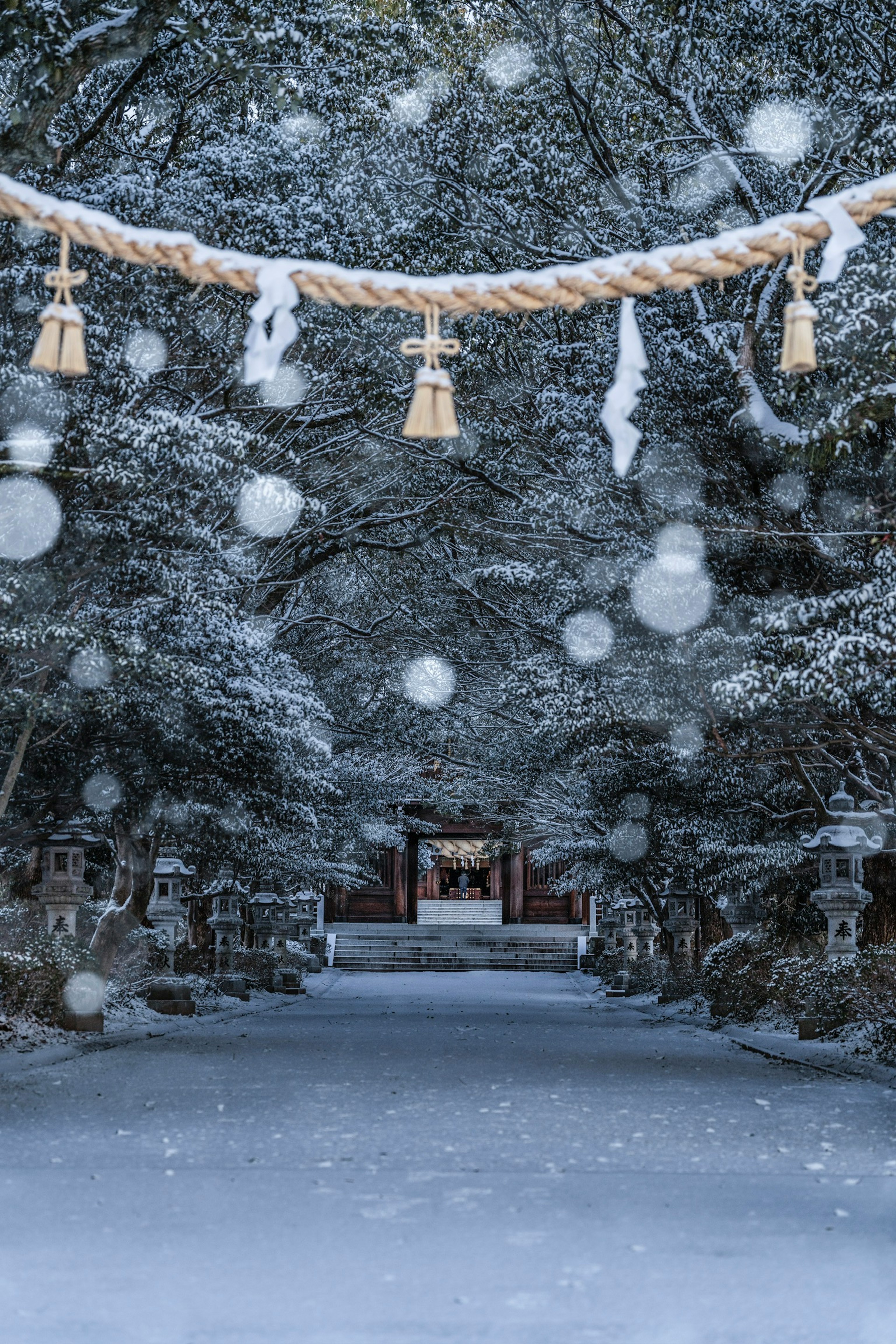 Snow-covered shrine path with hanging shimenawa and bells