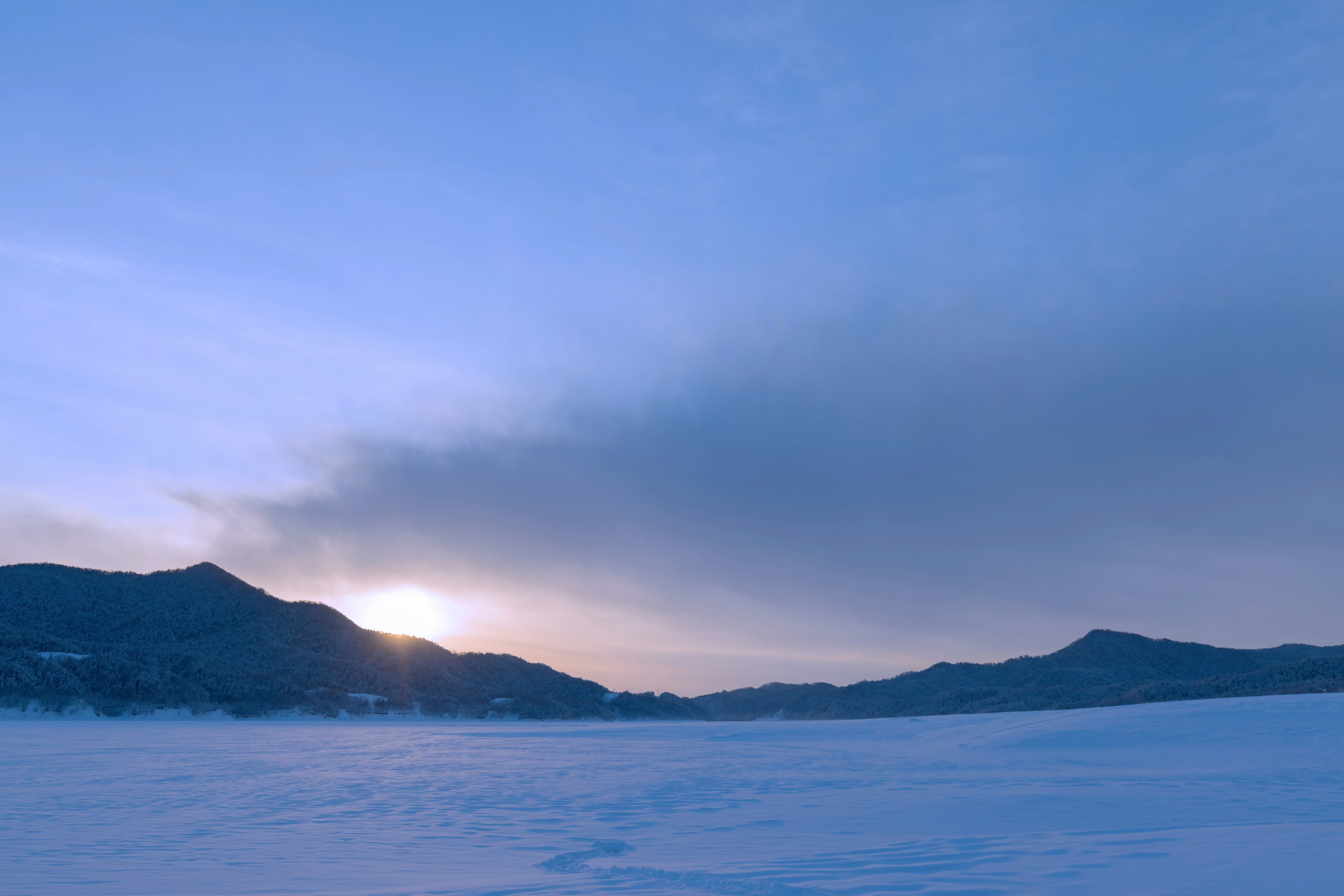 Sonnenuntergang über einer verschneiten Landschaft mit blauem Himmel