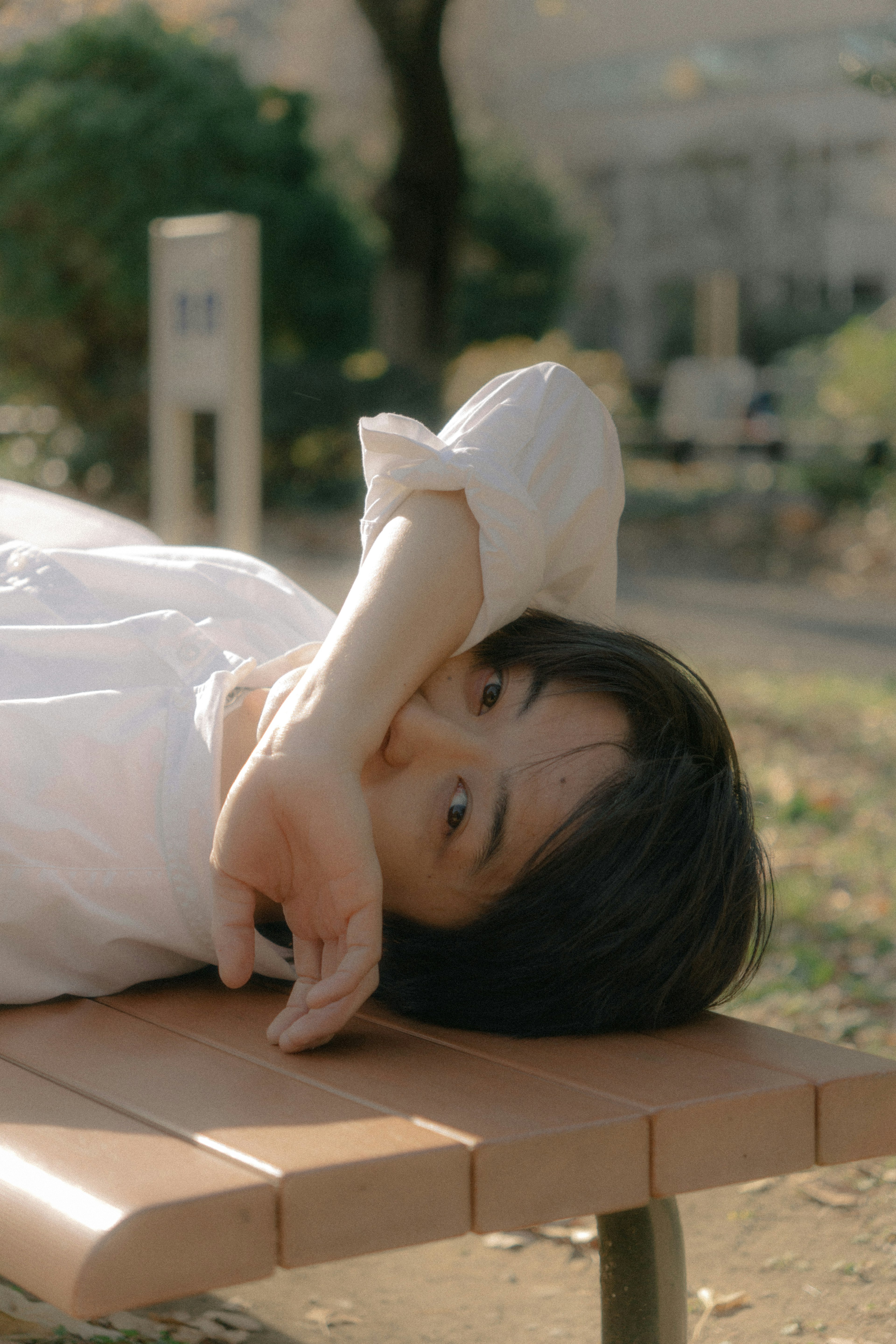 Young woman lying on a park bench wearing a white shirt relaxed expression in soft natural light