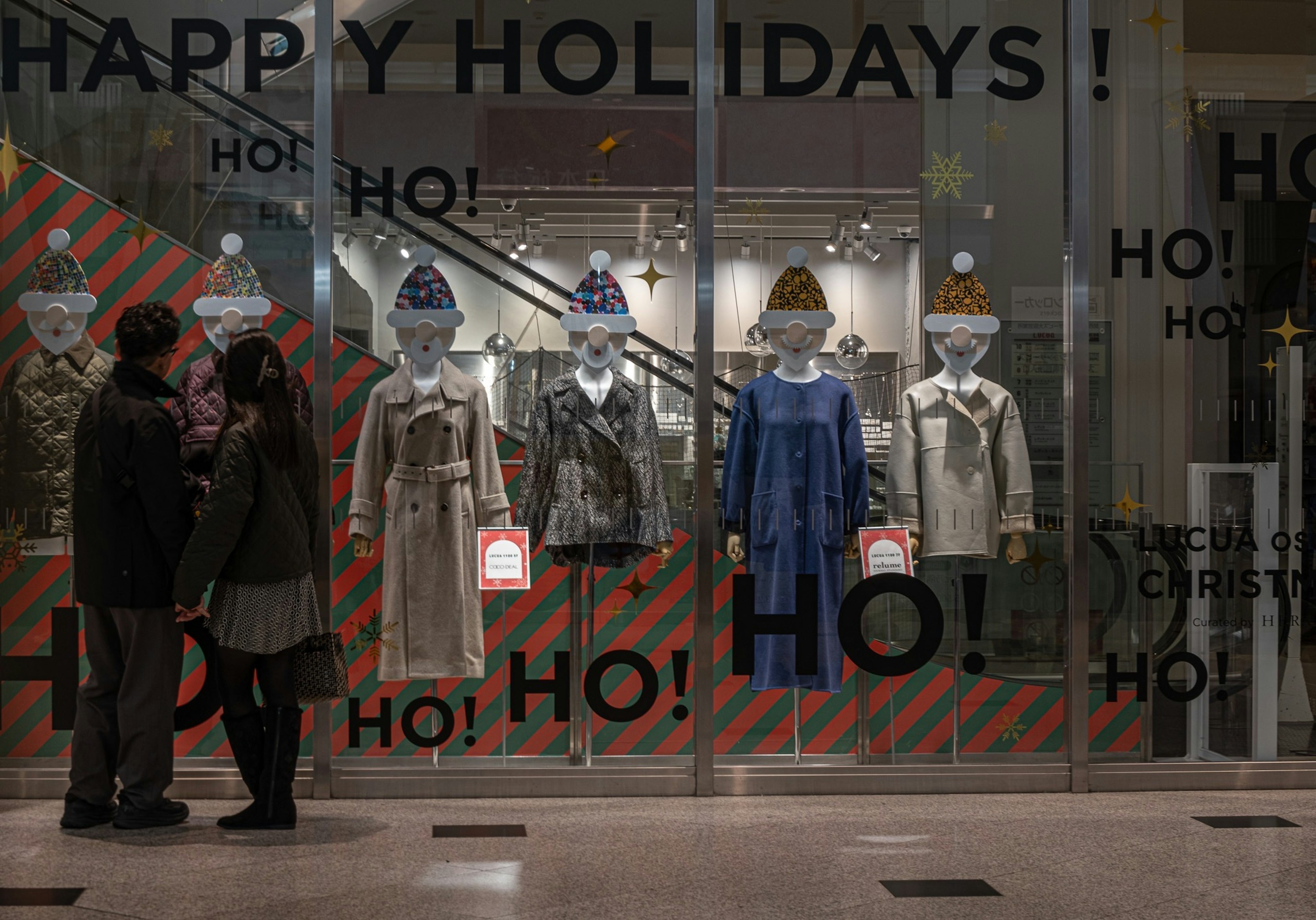 Couple devant une vitrine de magasin décorée pour les fêtes avec des vêtements festifs