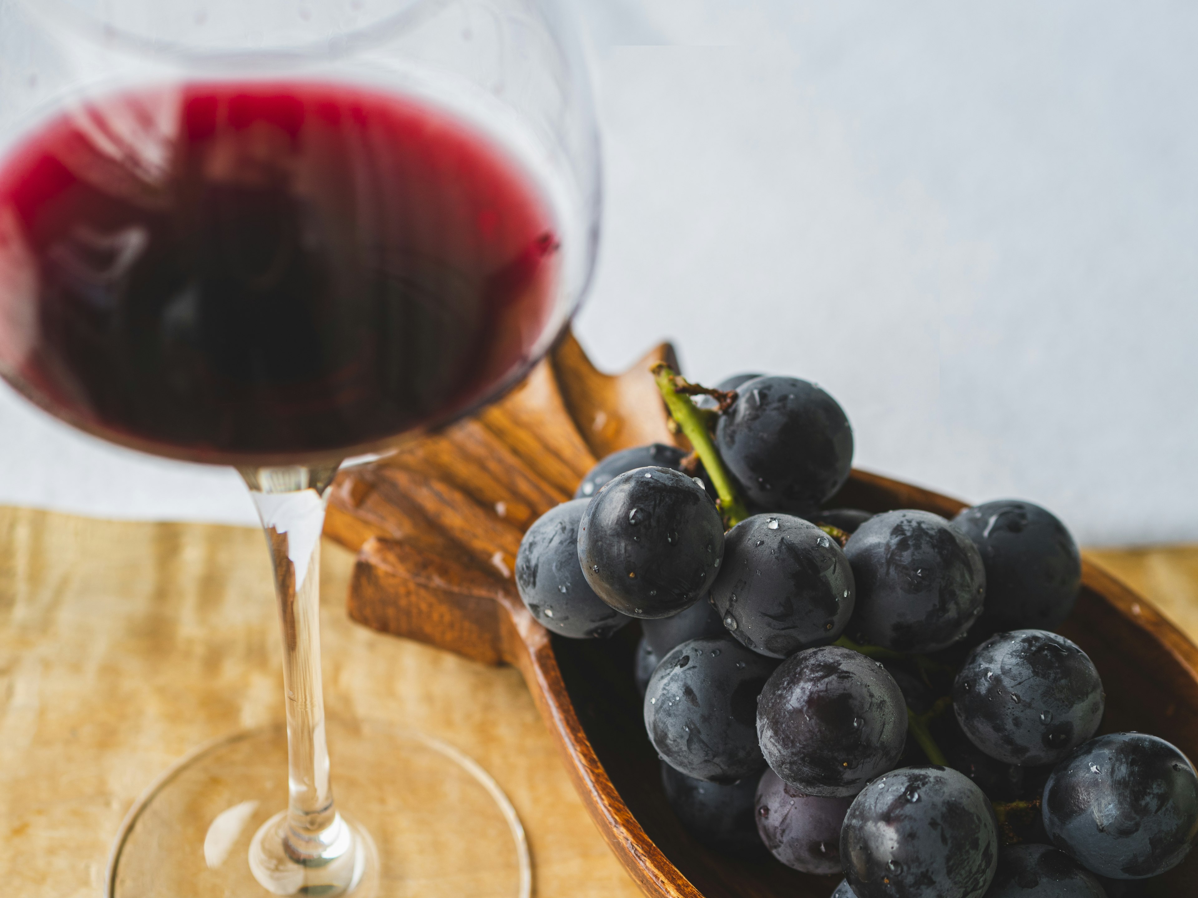 Image of a glass of red wine next to fresh grapes in a wooden bowl