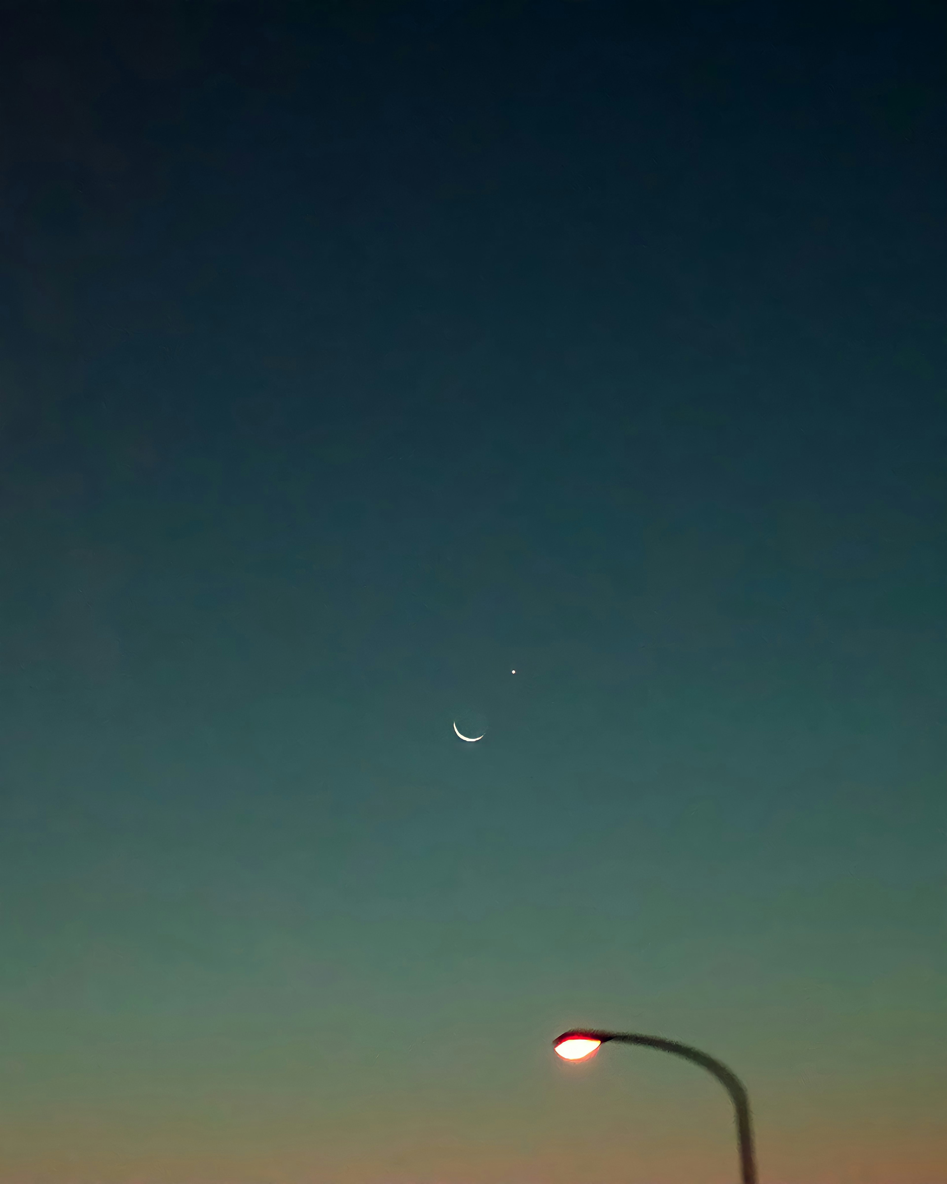 Silhouette of the moon and a star in the twilight sky with a streetlamp