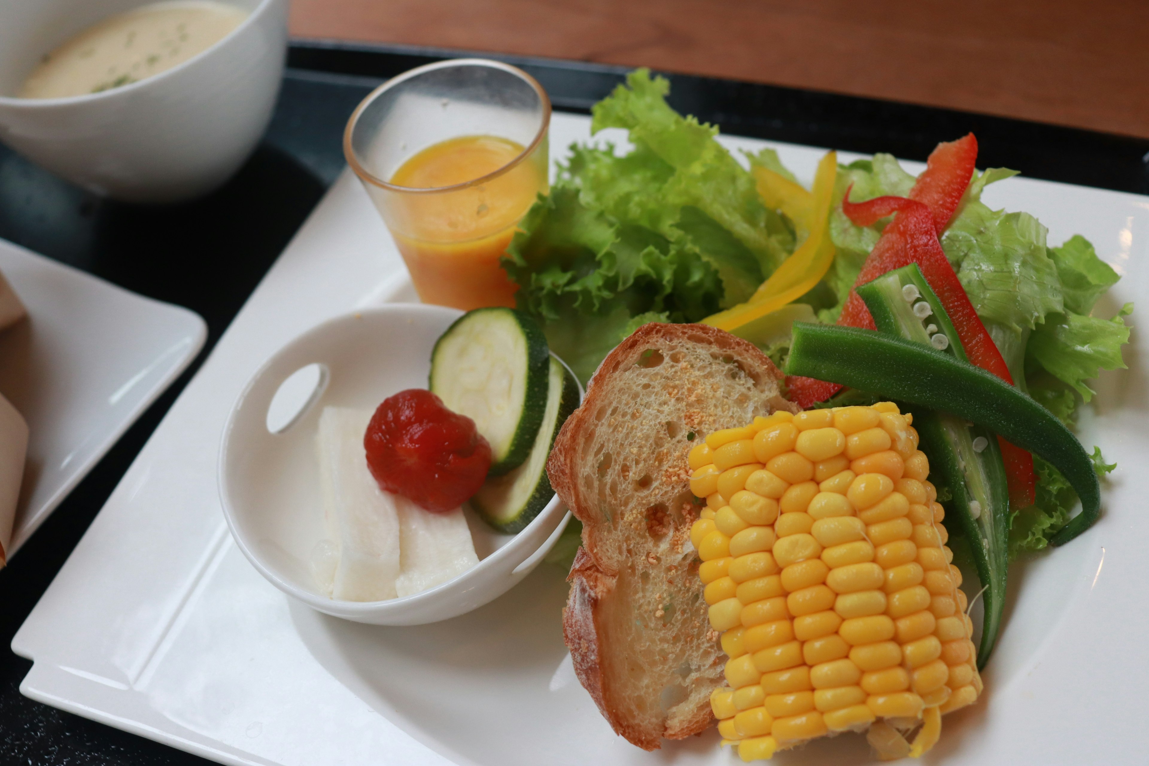 Une assiette colorée avec de la salade, du pain grillé, du maïs, une tomate cerise, un concombre et des poivrons