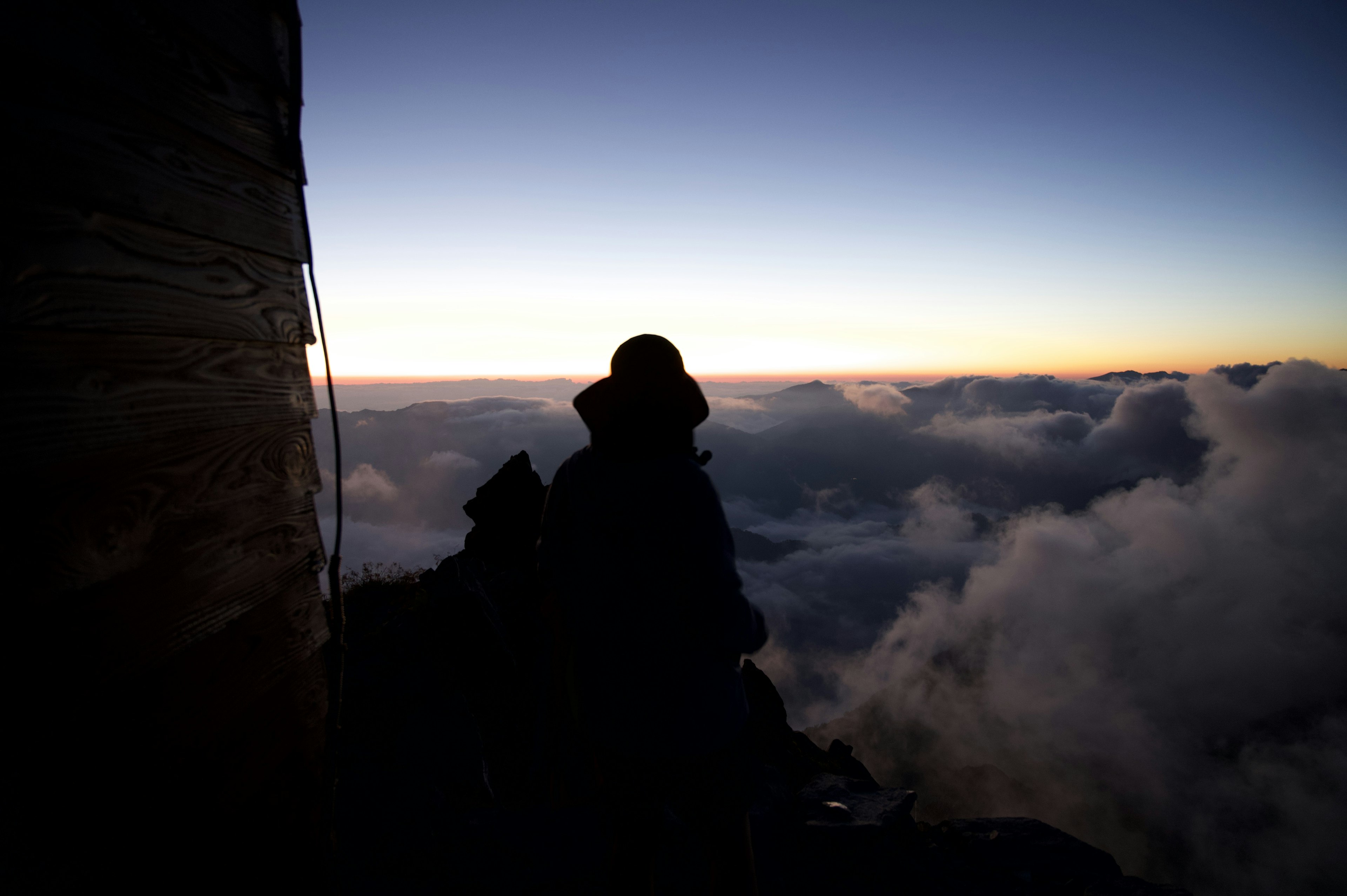 Siluet pendaki di atas awan dengan cahaya samar di cakrawala