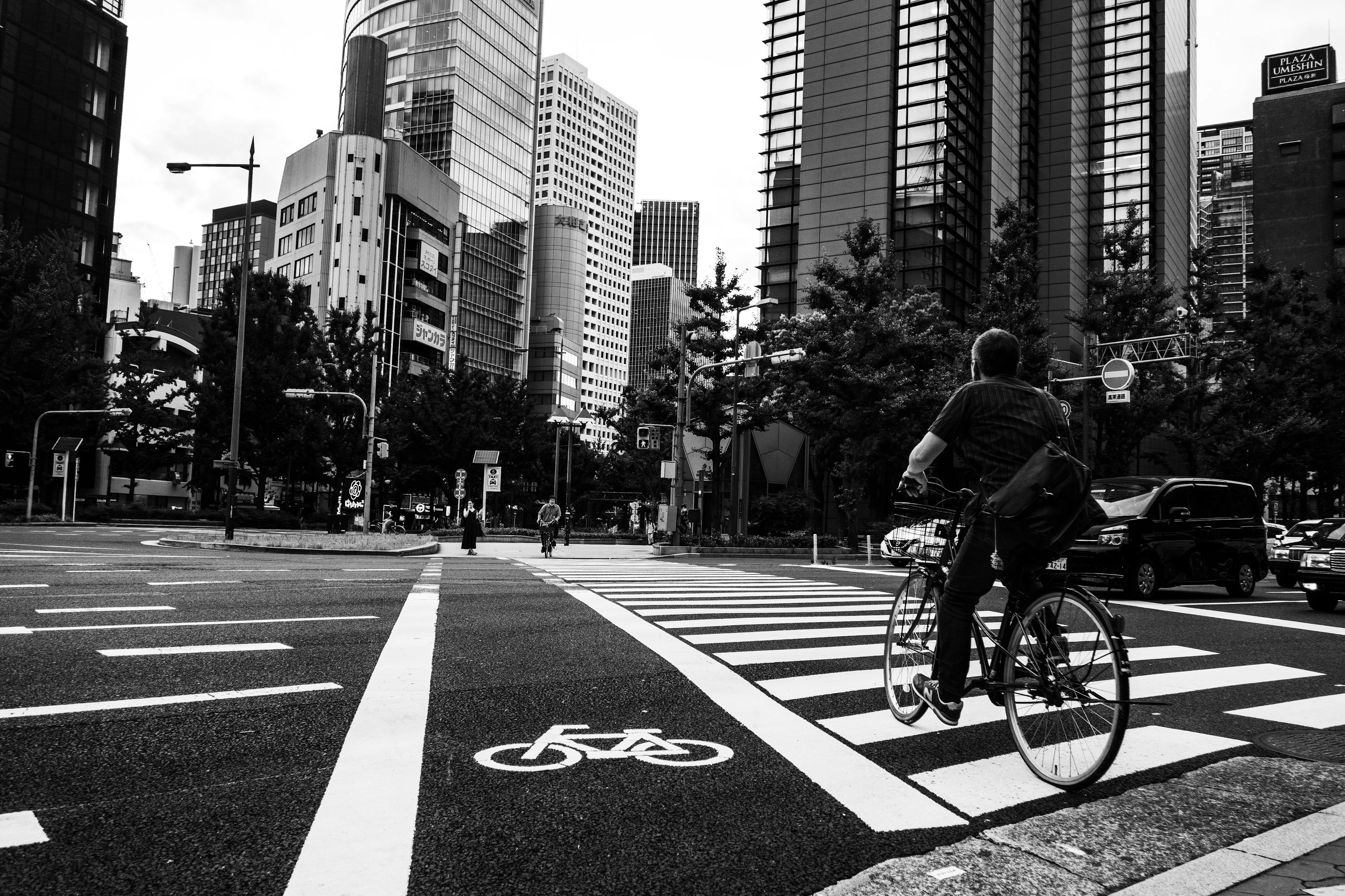 A man riding a bicycle at an urban intersection with skyscrapers