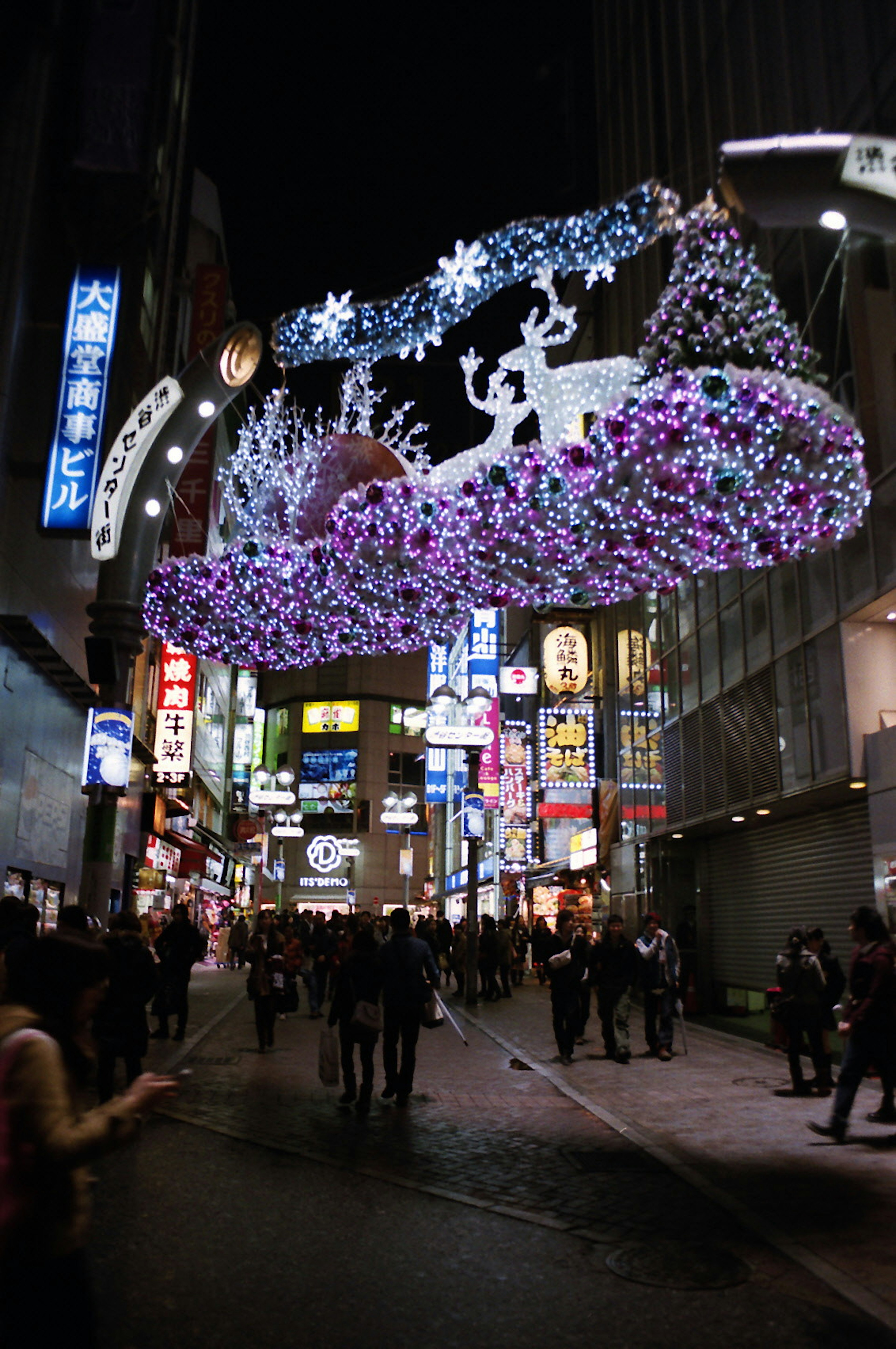 Luces navideñas vibrantes decorando una calle de la ciudad por la noche con peatones