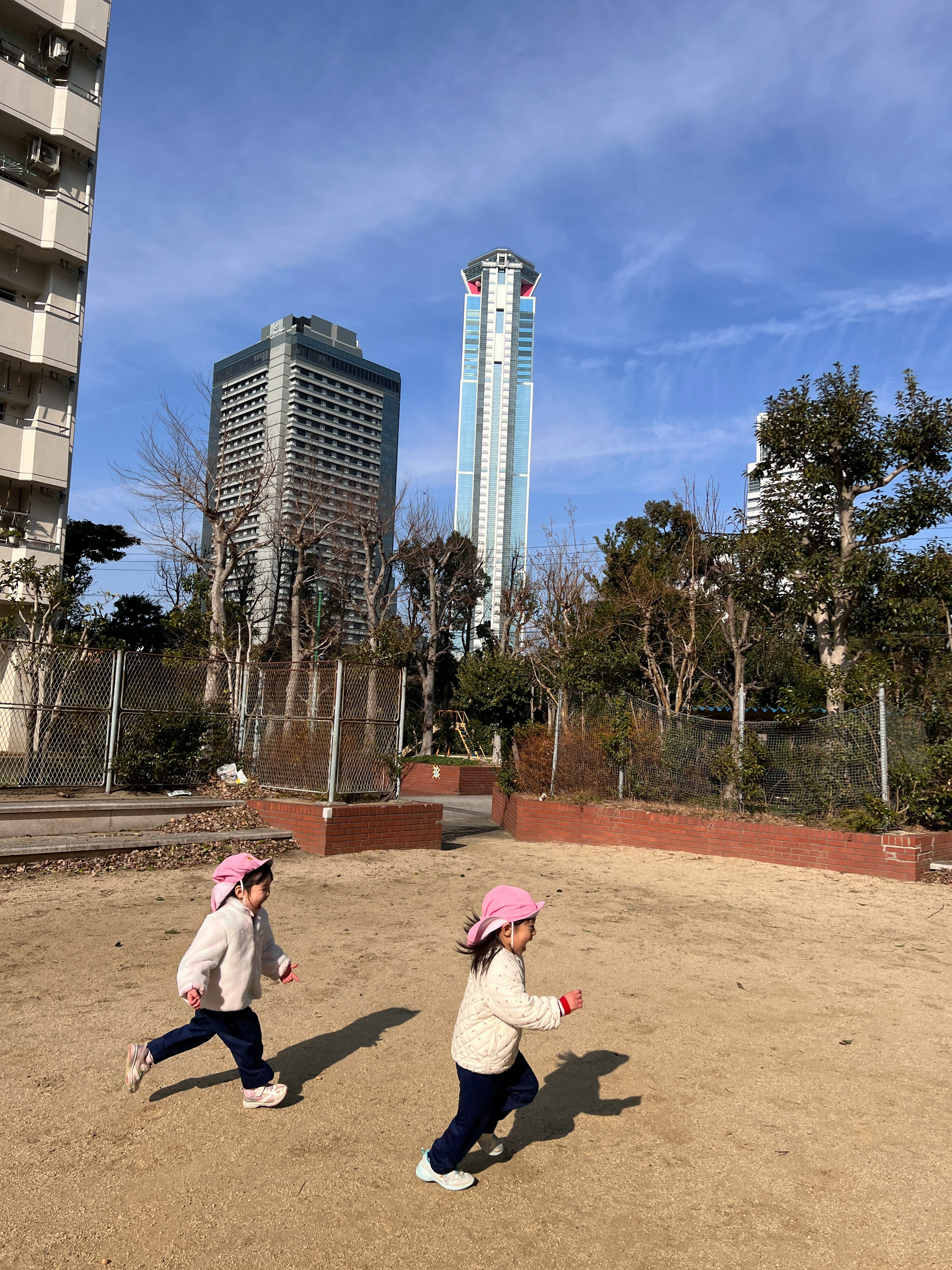 二人の子供が公園で遊んでいる様子 高層ビルと青空が背景にある