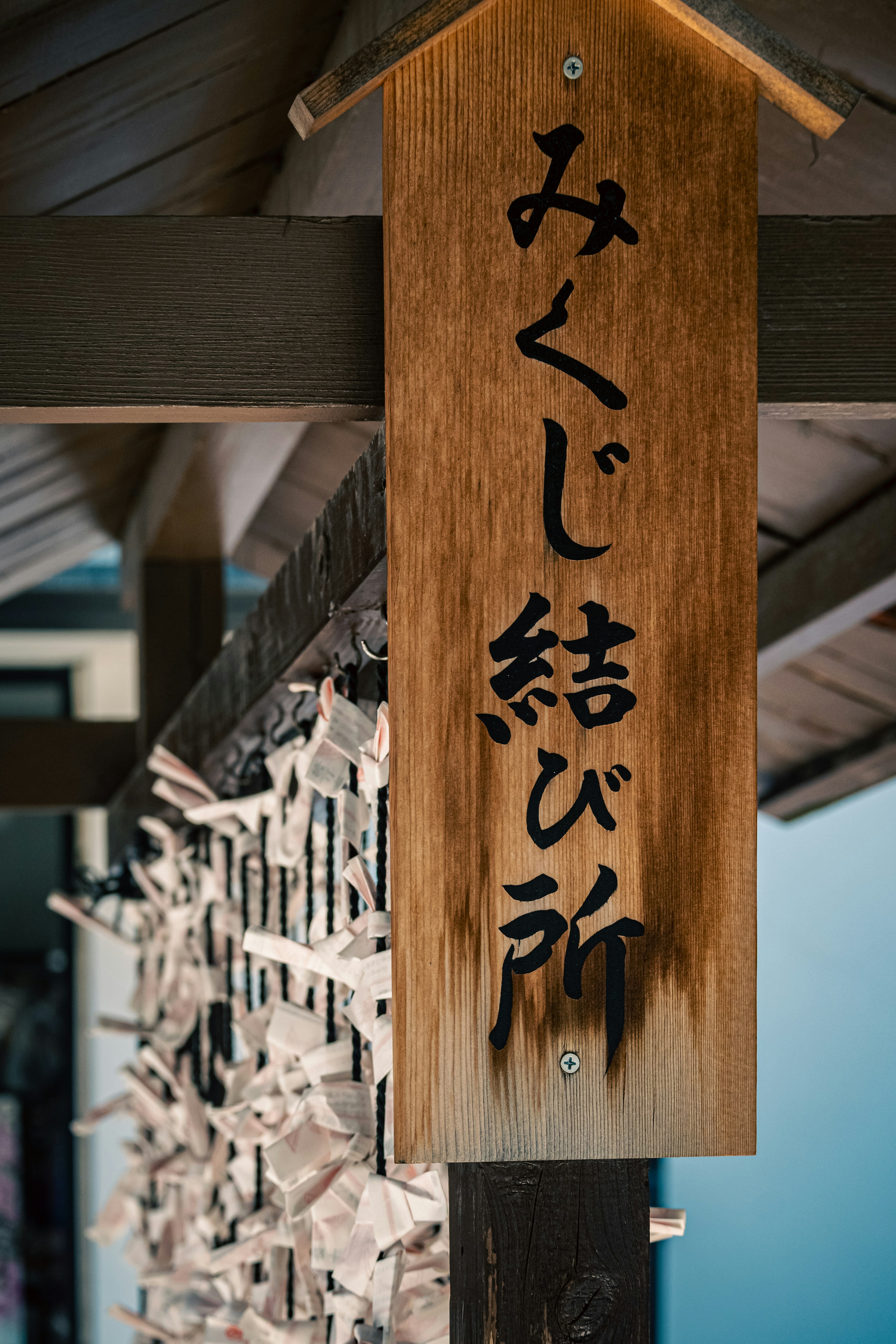 Wooden sign for the fortune-telling area with hanging white omikuji